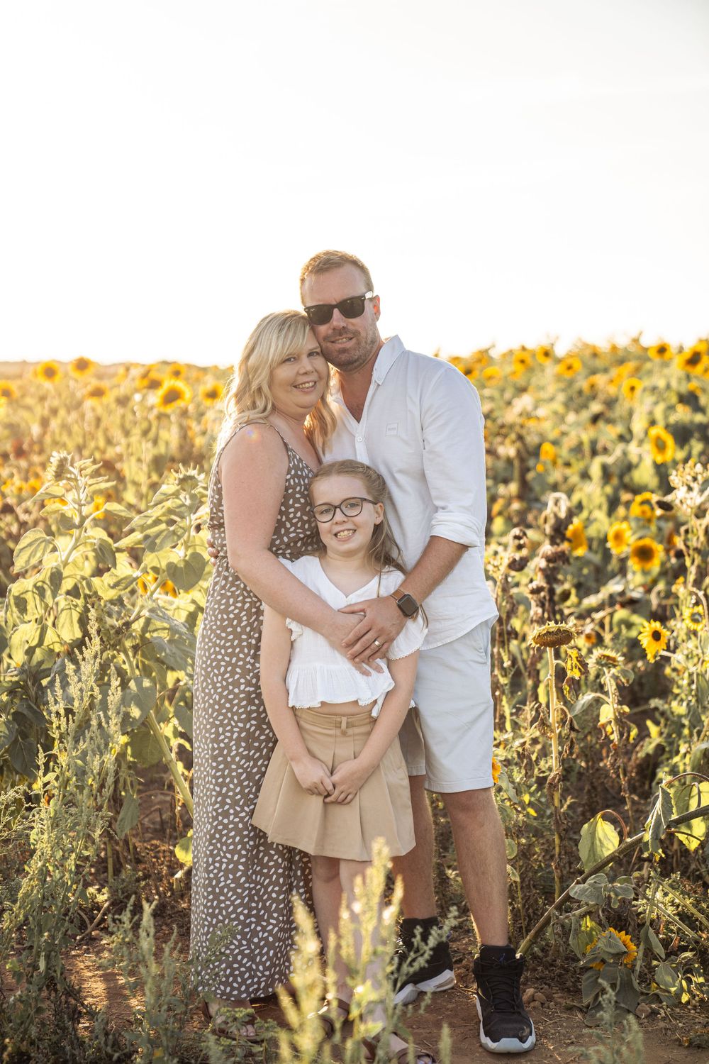 A family poses together in a beautiful sunflower field during golden hour sunset.