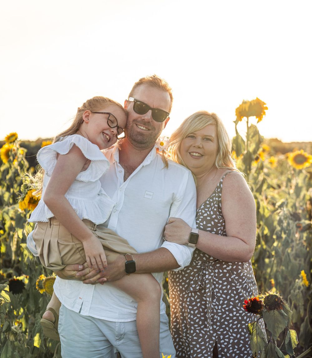A joyful family shares a candid moment while posing in a golden sunflower field during sunset.
