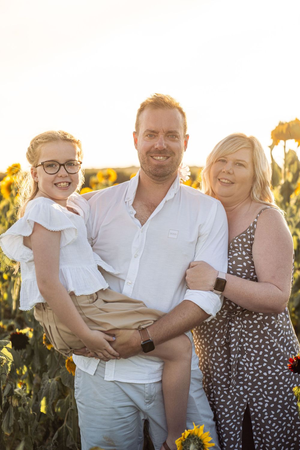 A loving family embraces and smiles together in a sunlit sunflower field at golden hour.