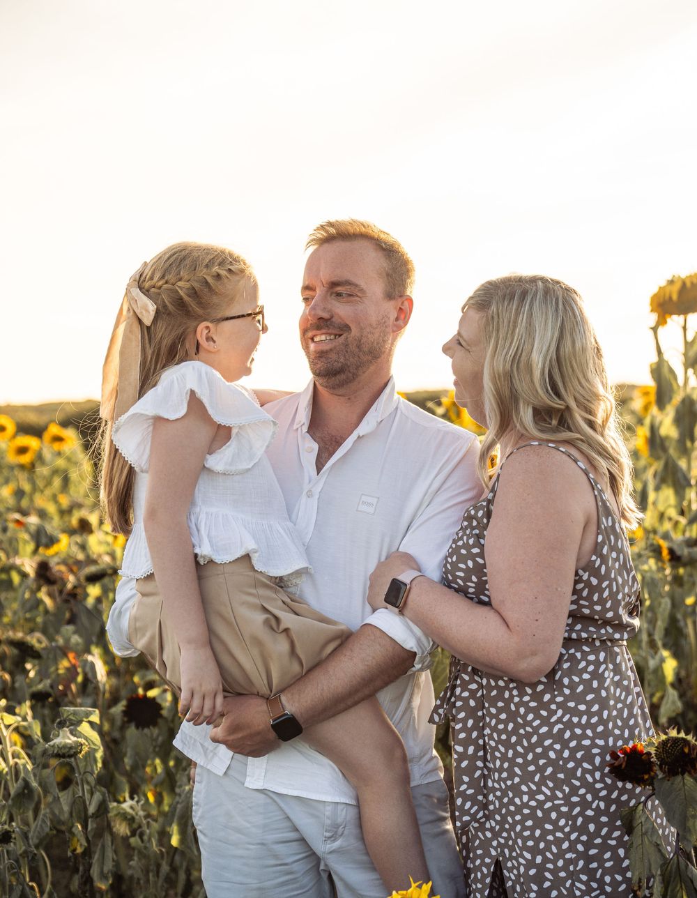 Family embraces together in golden sunflower field at sunset creating joyful candid moments.