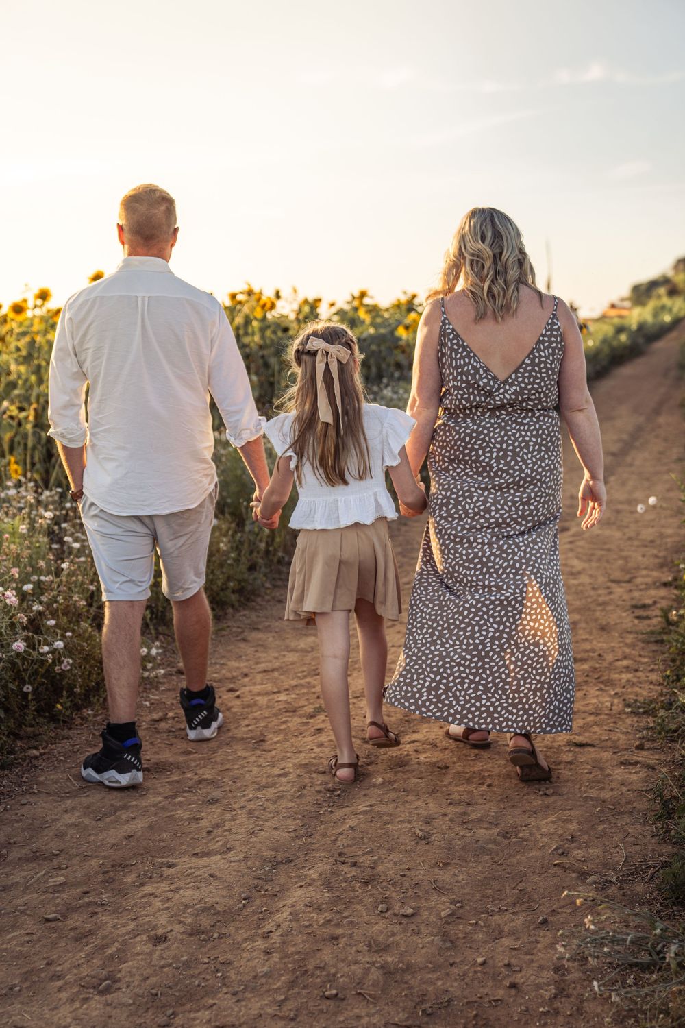Family walking together through a sunflower field at sunset, photographed from behind in a series of candid shots.