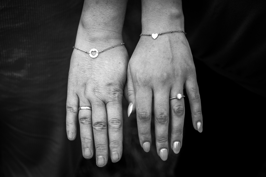 Zwart-wit detailfoto van twee handen met sieraden, verbonden door een armband.