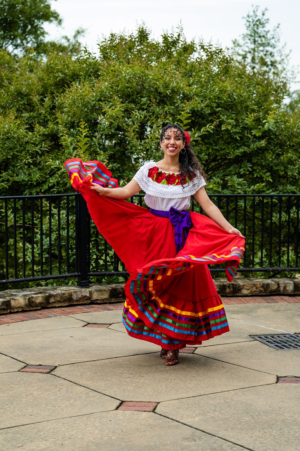 Graduate performs celebratory dance in traditional red and white cultural dress on outdoor patio.
