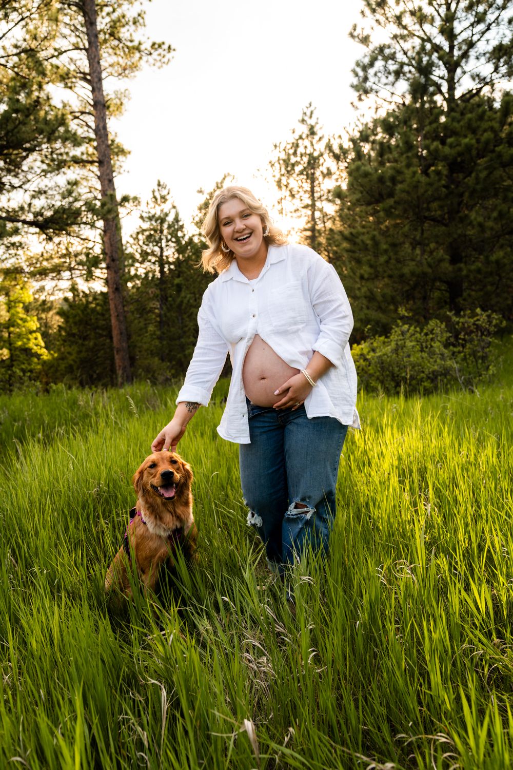 A person in a white shirt and jeans plays with a brown dog in a grassy field at sunset.