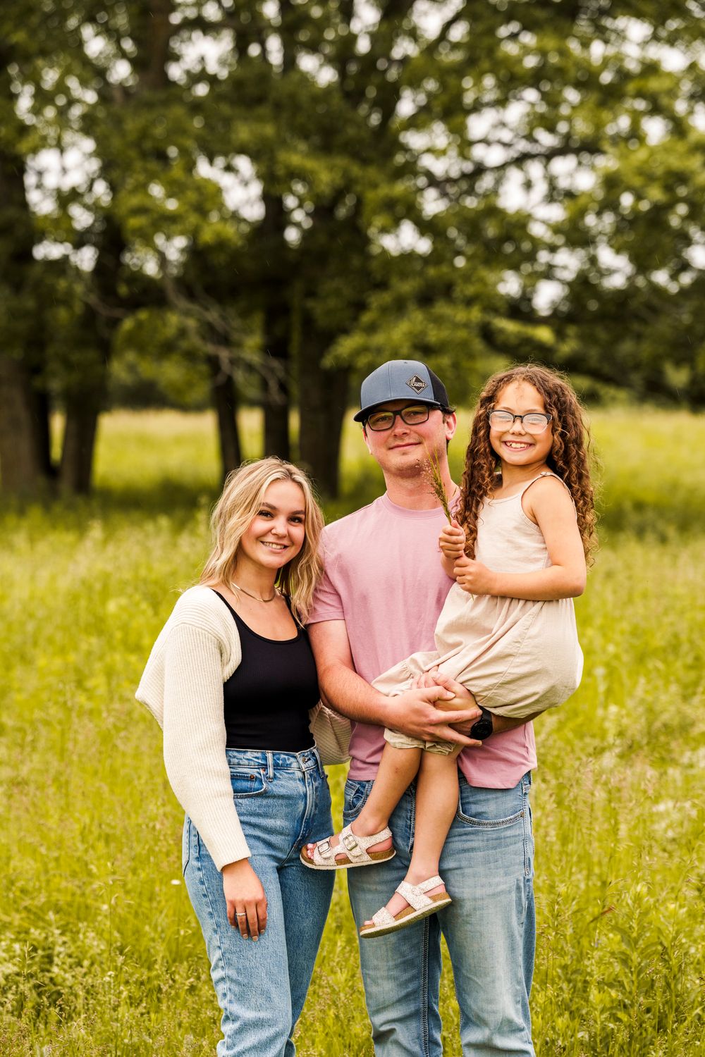 A family portrait taken in a sunny meadow with trees in the background.