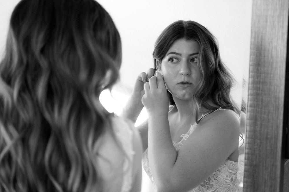 A reflection shows someone putting on earrings while getting ready.