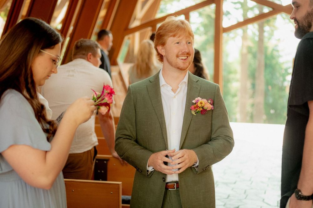Wedding party members gather in a sunlit room with floral bouquets.