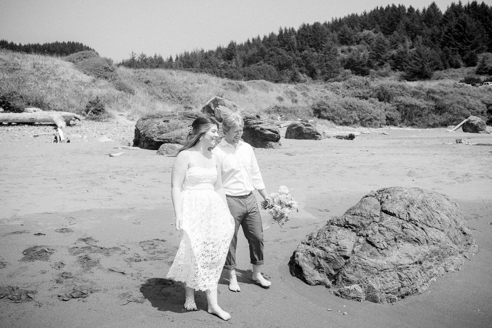 Wedding couple walking along a scenic coastal beach with dramatic cliffs in black and white.