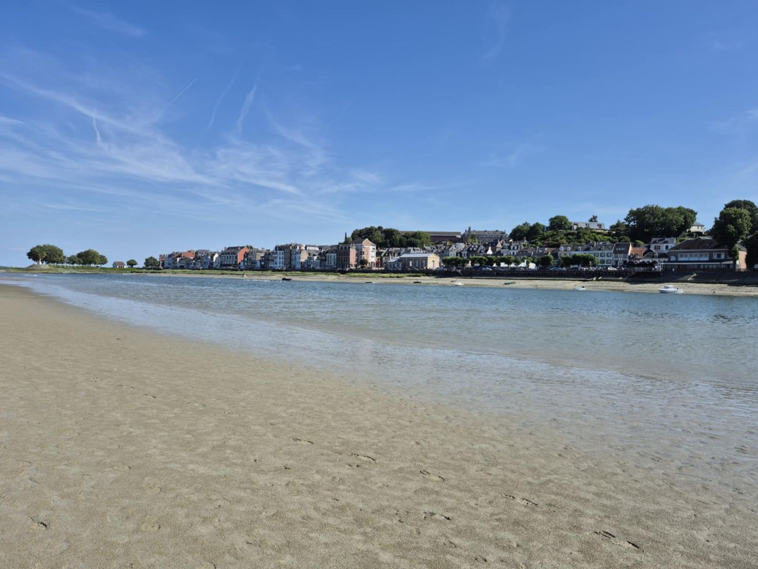Tranquil beachfront with calm blue waters and coastal homes lining the shore under a bright sunny sky.