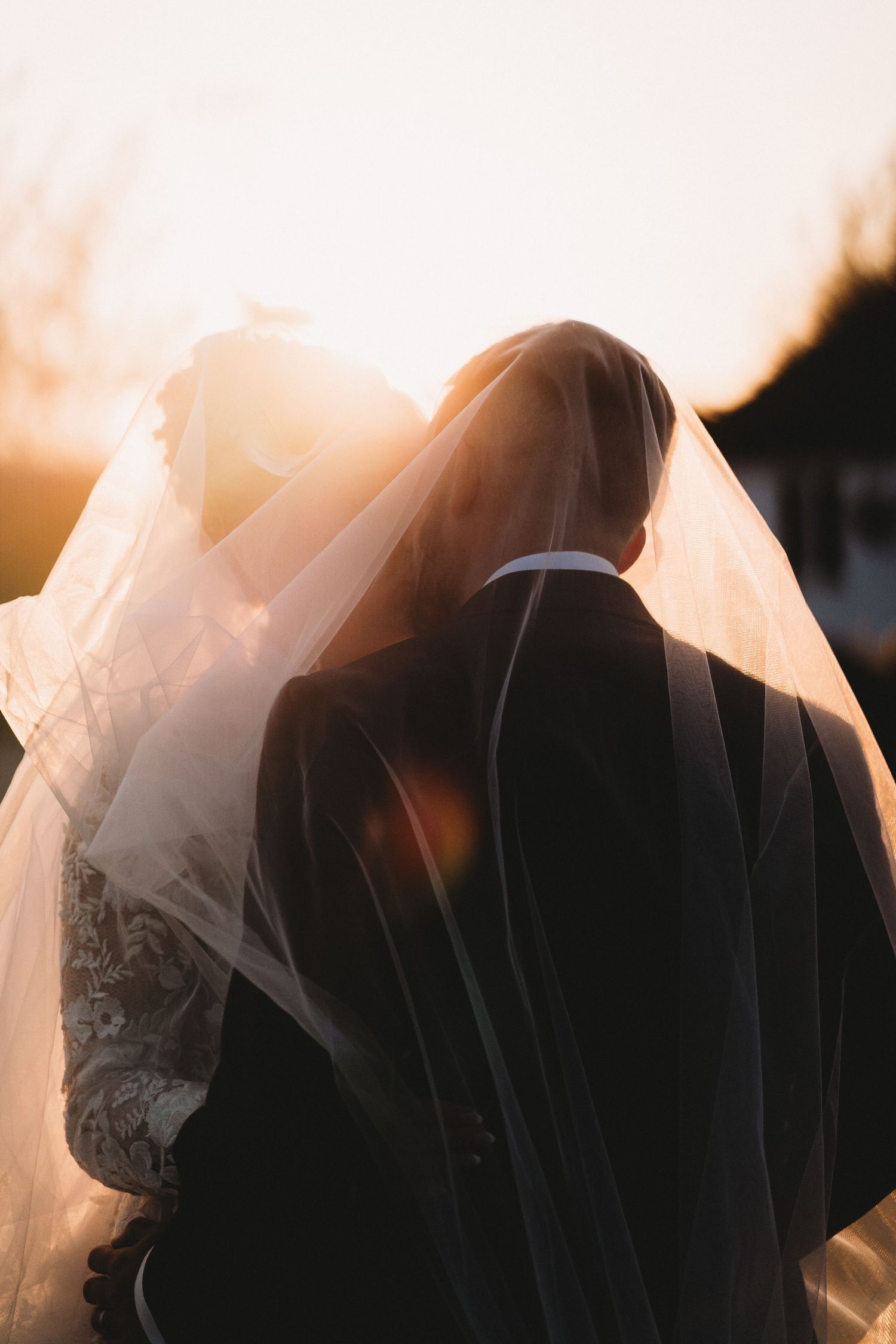 A romantic silhouette of a bride and groom embracing during golden hour with sunlight streaming through the wedding veil.