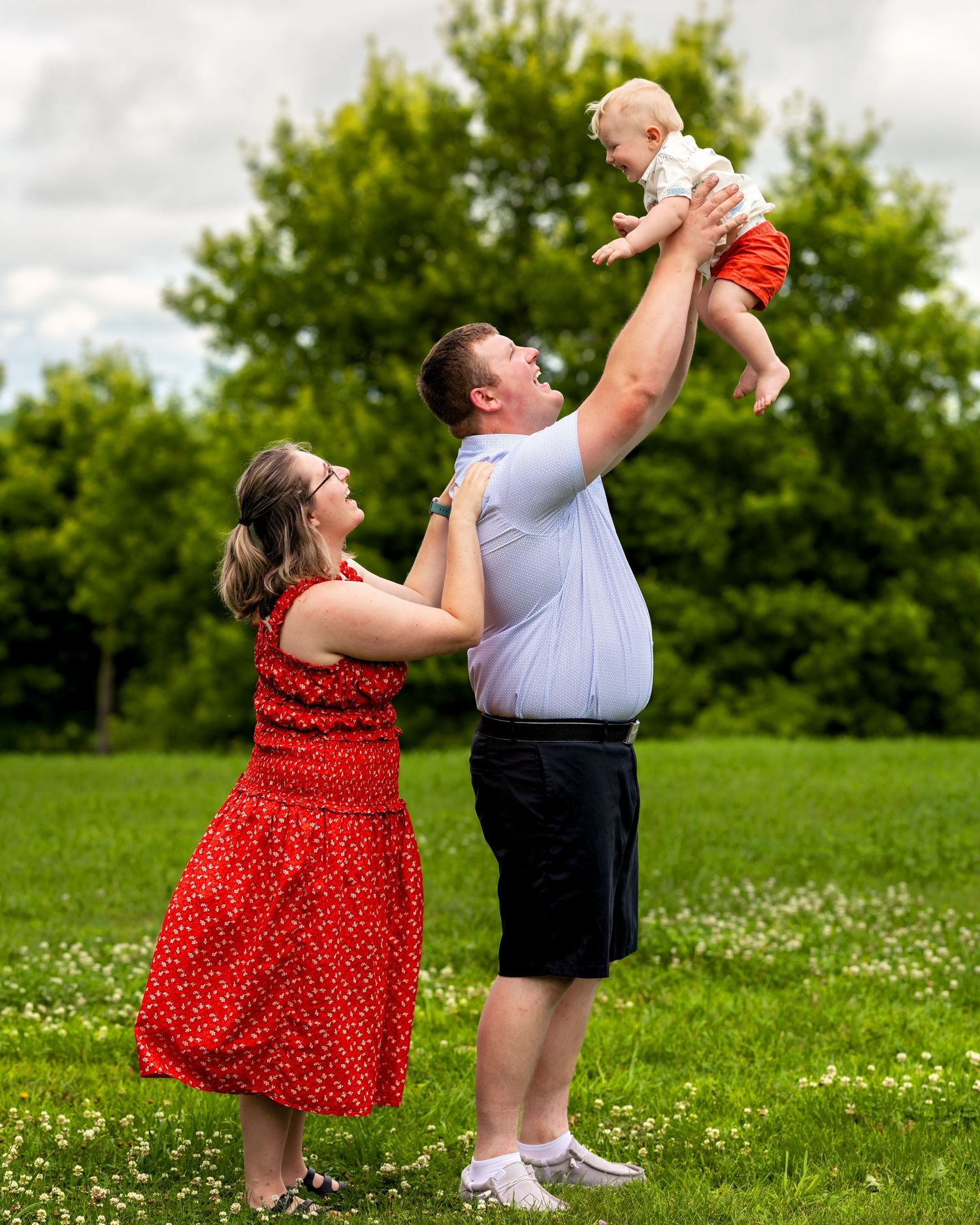 Family of four smiles together outdoors during a fall portrait session in a wooded setting.