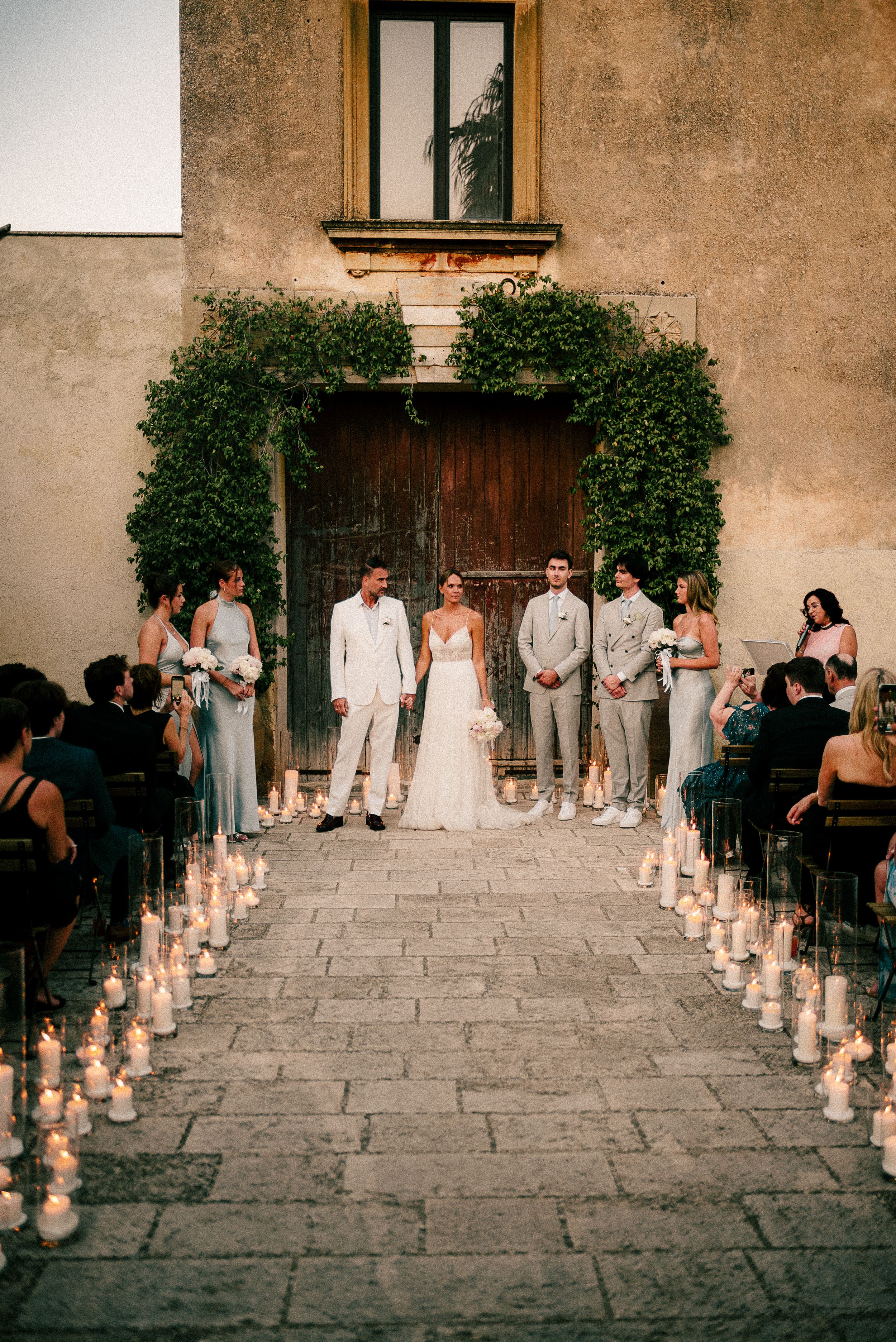 Romantic wedding ceremony setup with rows of glowing lanterns lining a stone pathway at dusk.