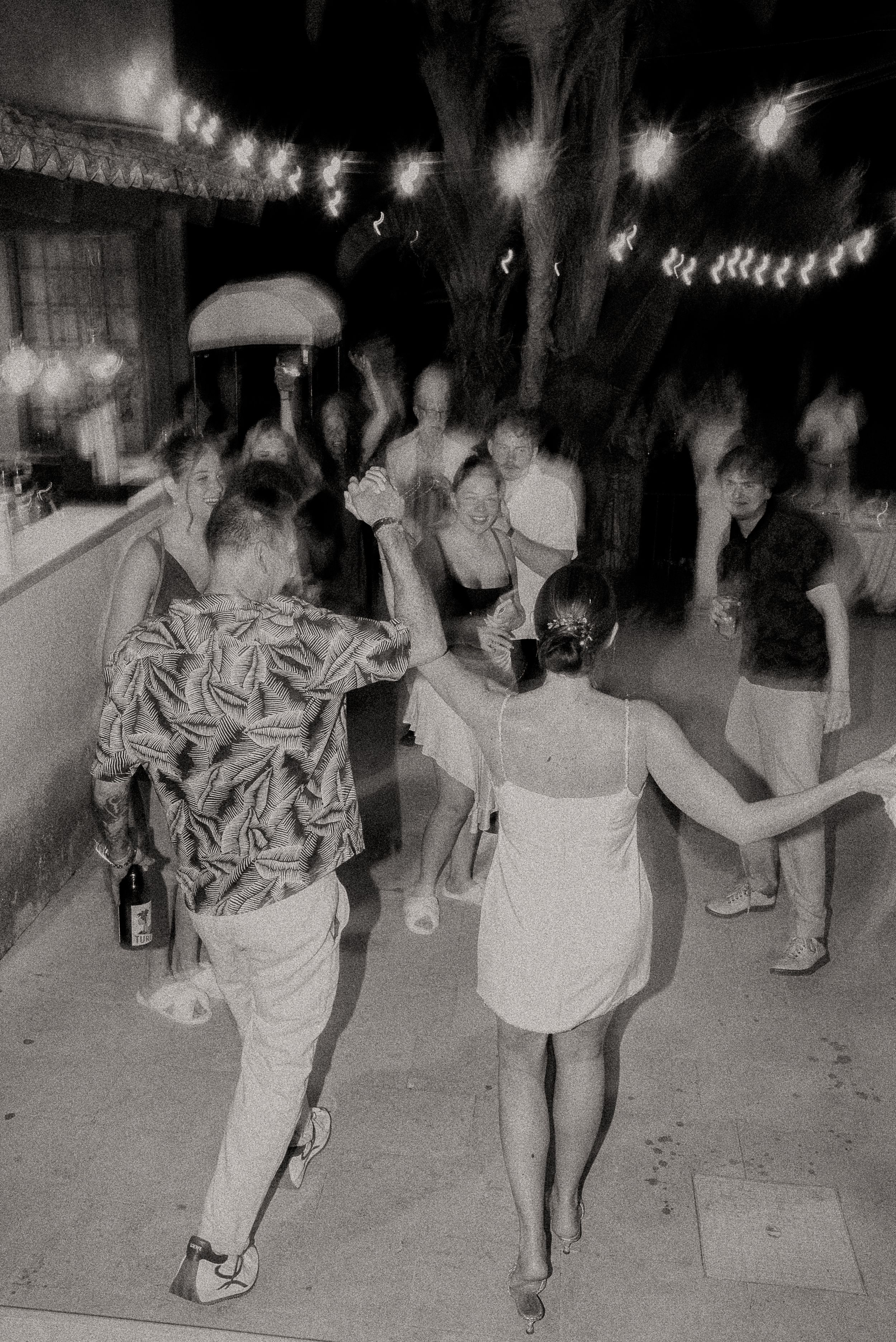 Black and white photo of guests dancing at an outdoor party under string lights.