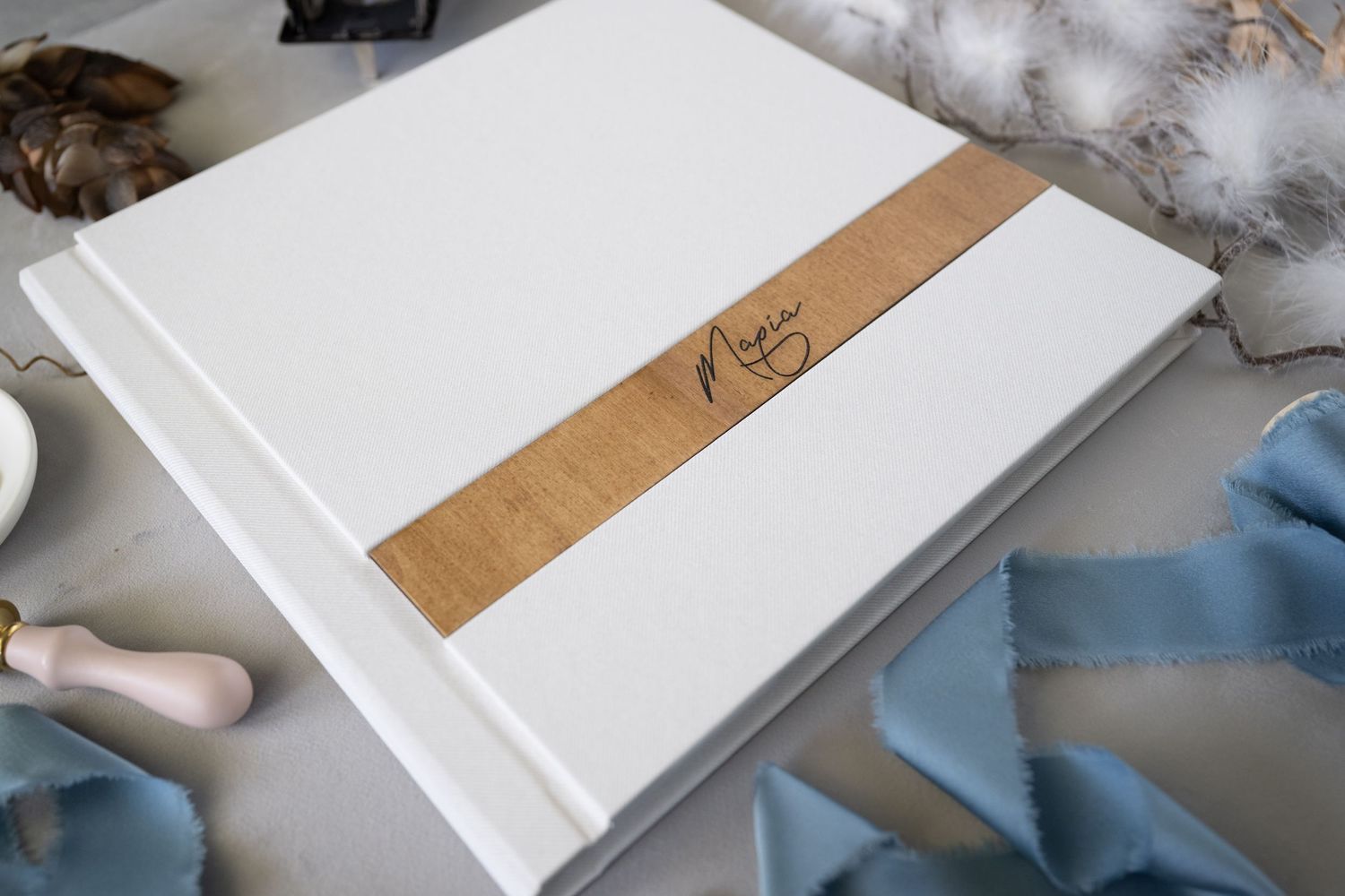 A white wedding album with a tan leather accent strip and the word 'Mr' etched on it rests on a soft surface.