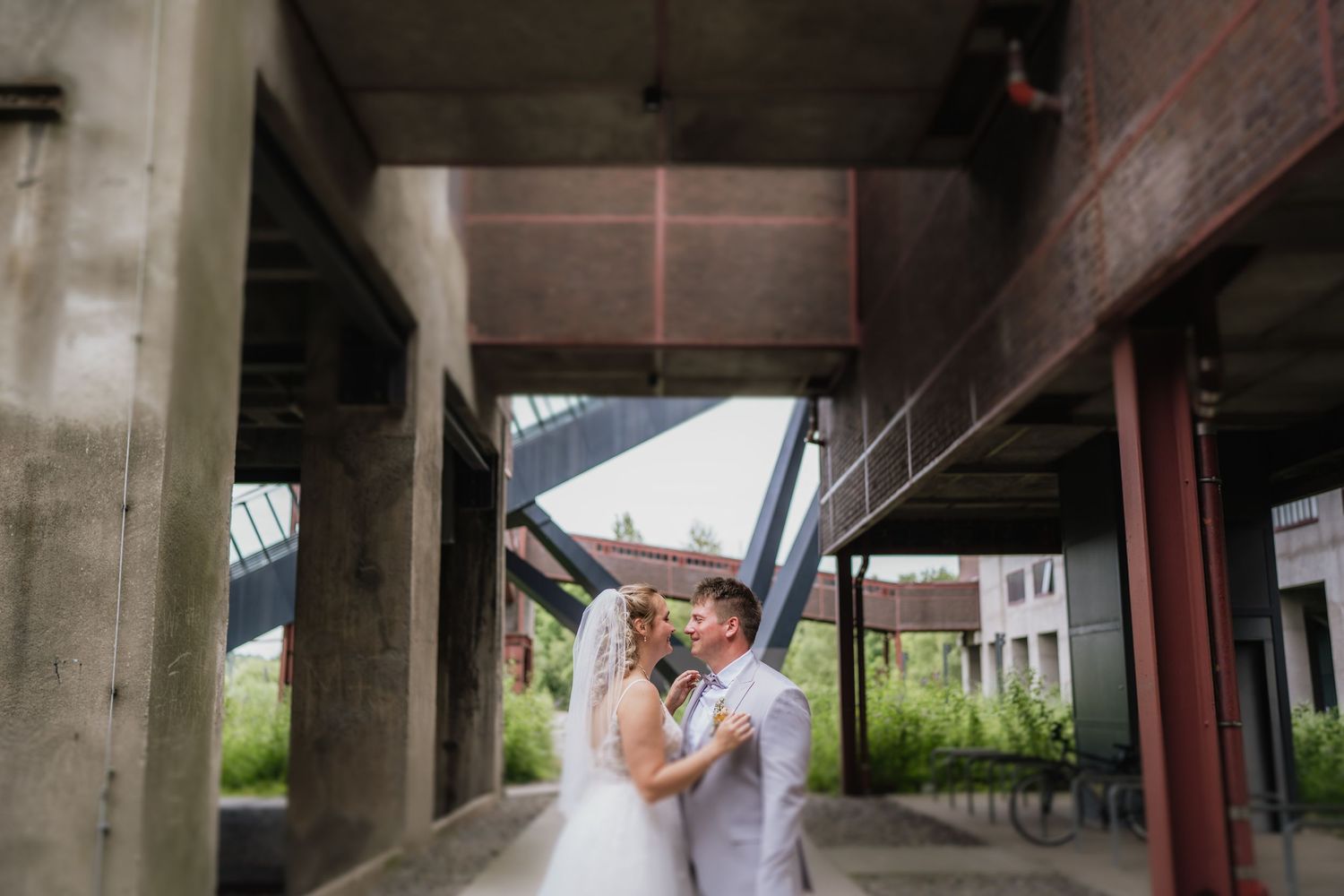 A couple embraces under an industrial concrete structure on their wedding day.