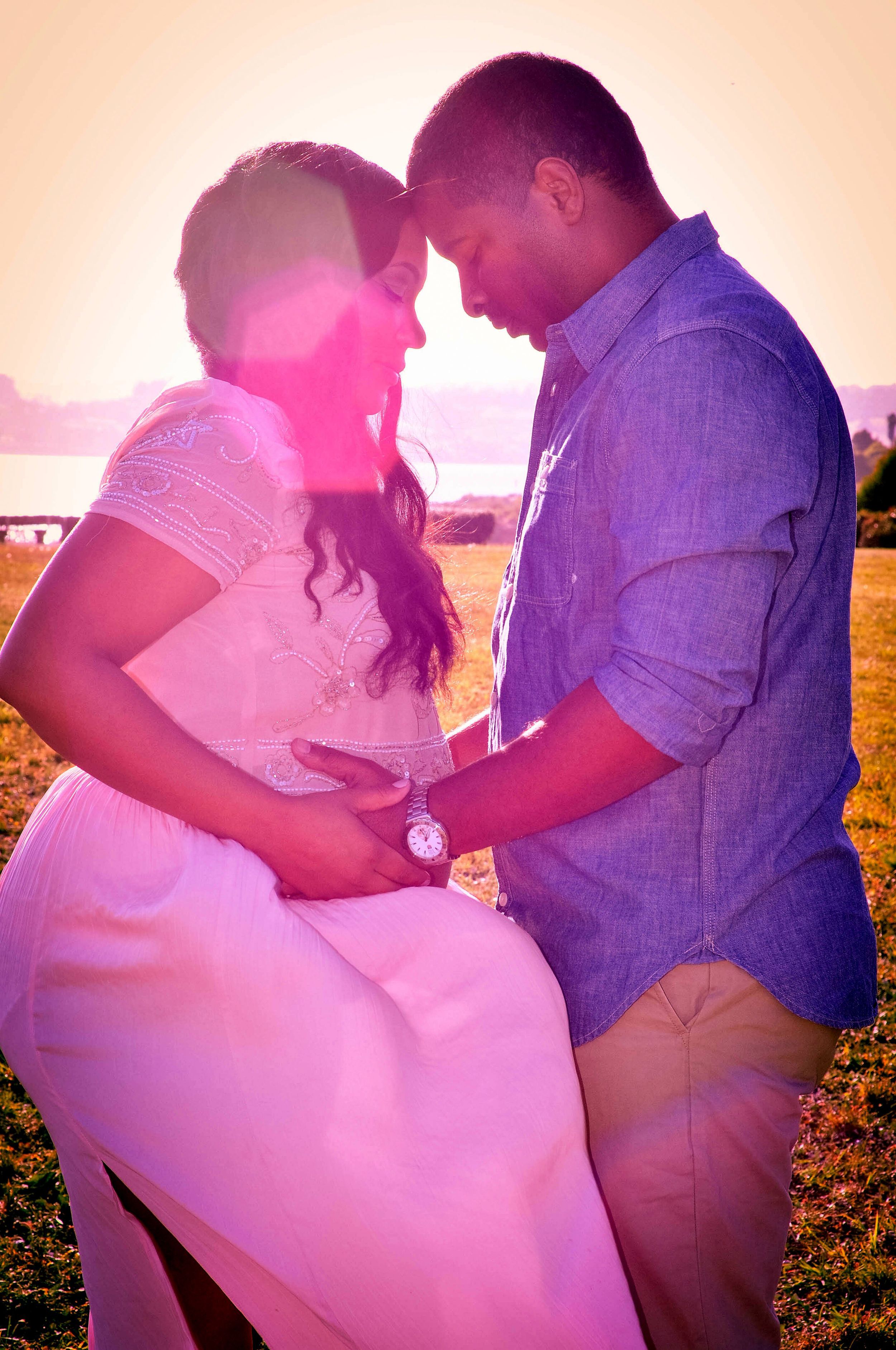 A romantic couple embraces outdoors during sunset with warm pink lighting creating a dreamy atmosphere.
