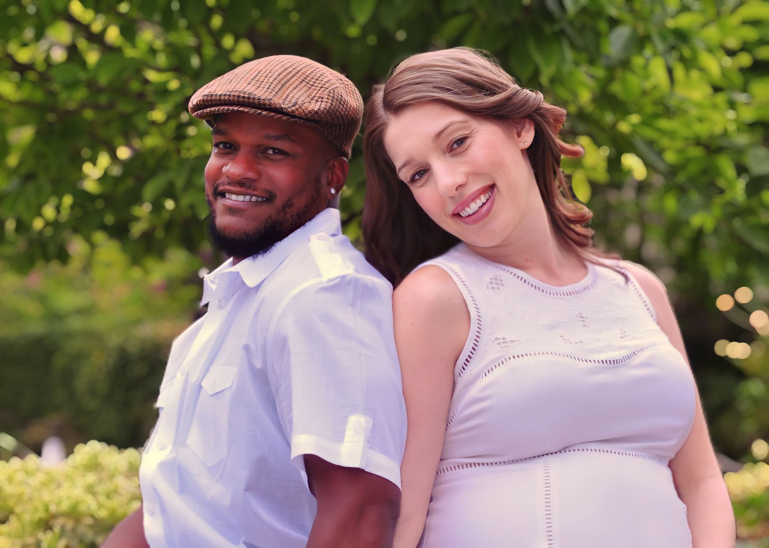 Two people smile while posing outdoors together on a sunny day surrounded by greenery.