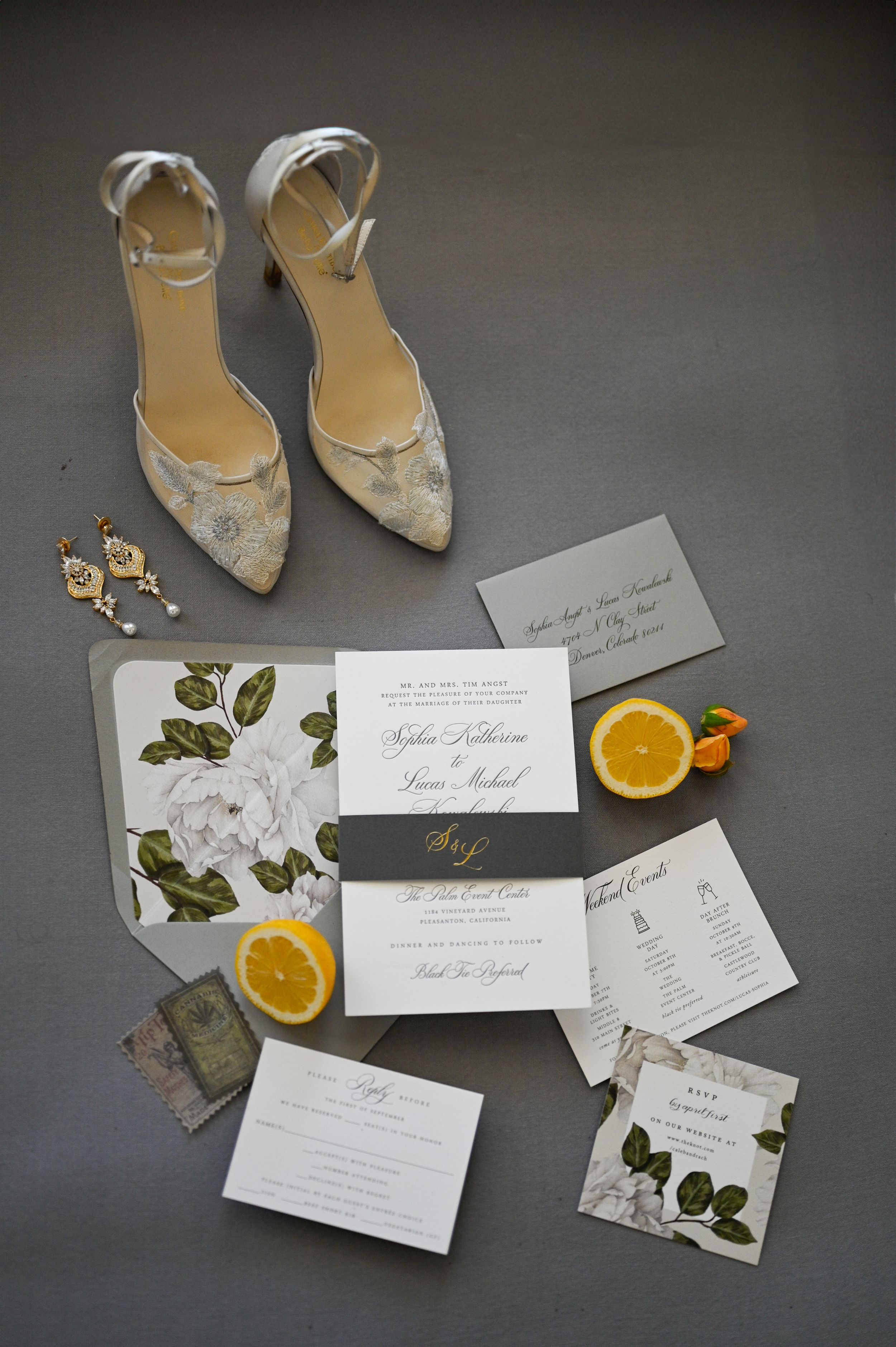 Wedding stationery and elegant bridal shoes arranged with orange slices on dark surface.