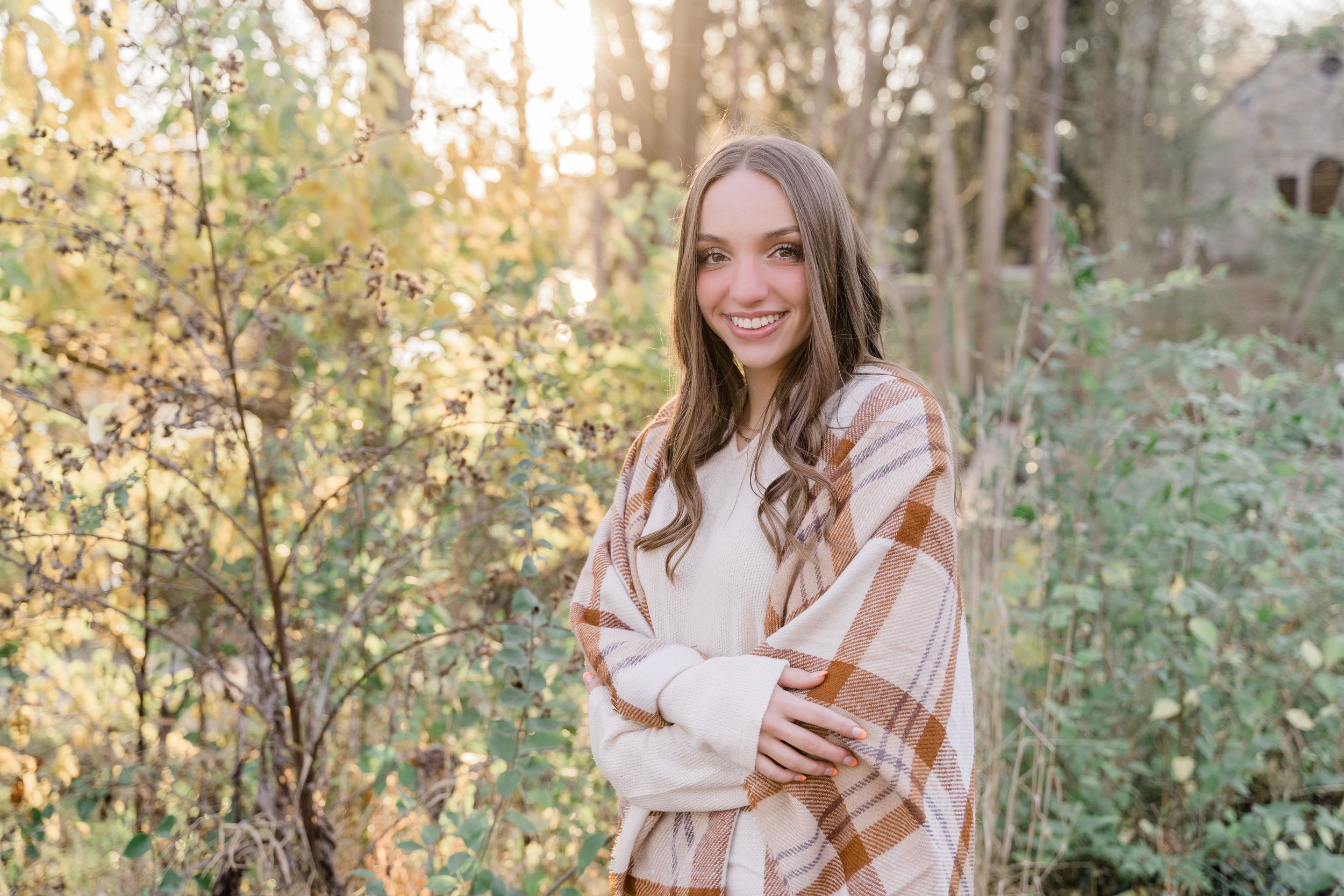 Candid fall photo session in a sun-drenched forest with warm autumn colors and brown plaid blanket details.