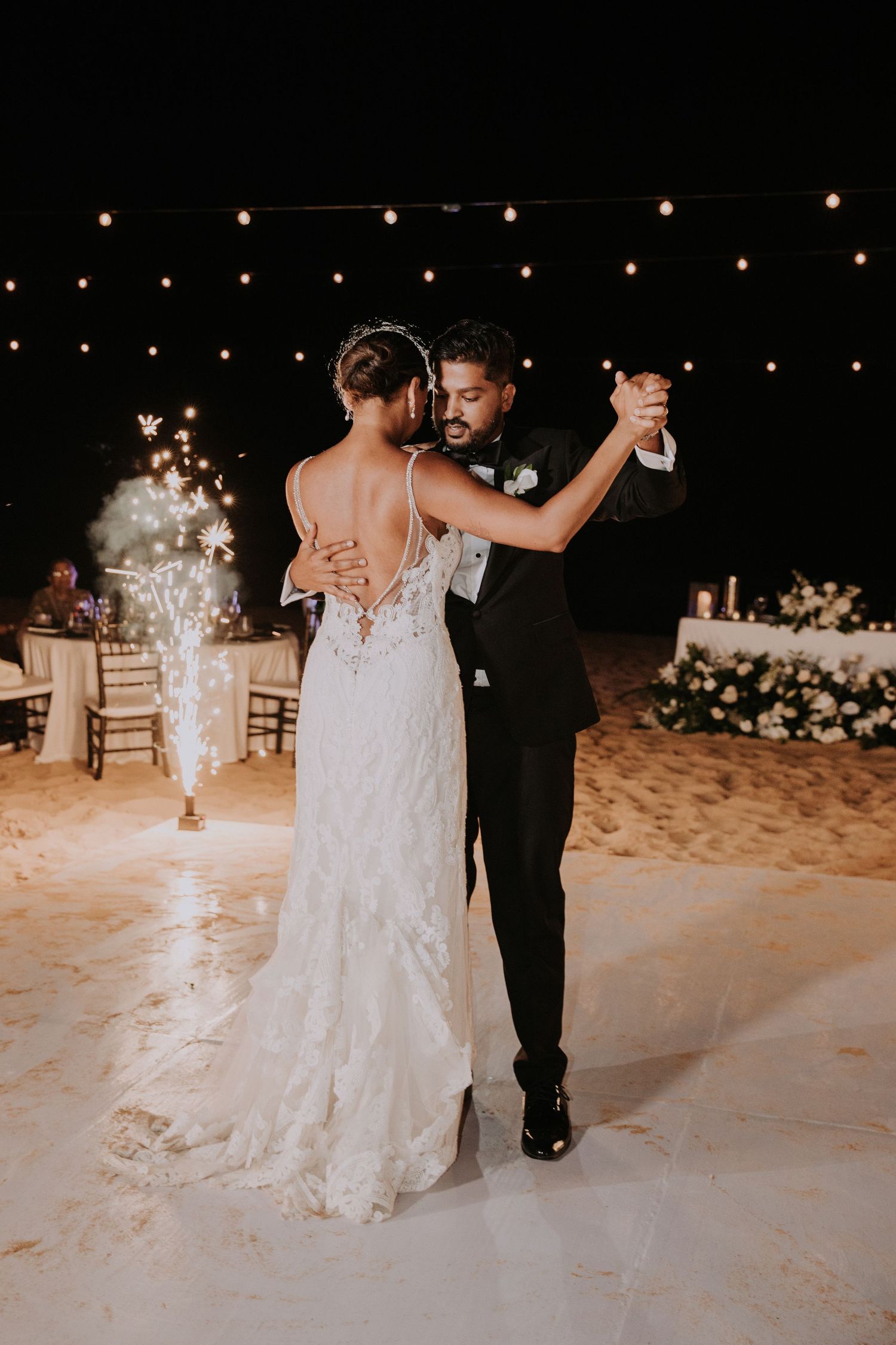 Couple dances together on illuminated outdoor dance floor in formal wedding attire.