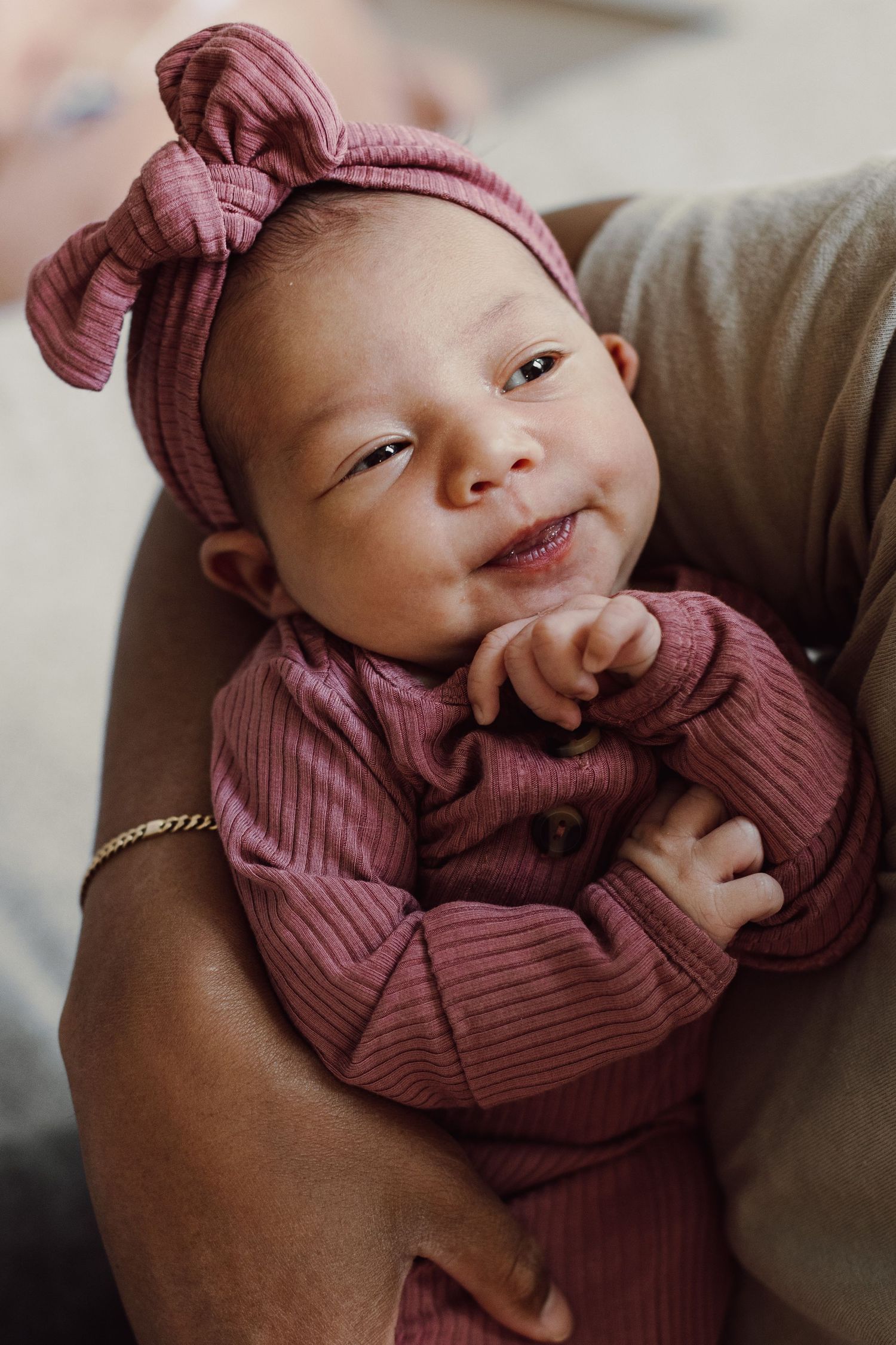 Baby wearing pink ribbed outfit with bow headband being held lovingly.