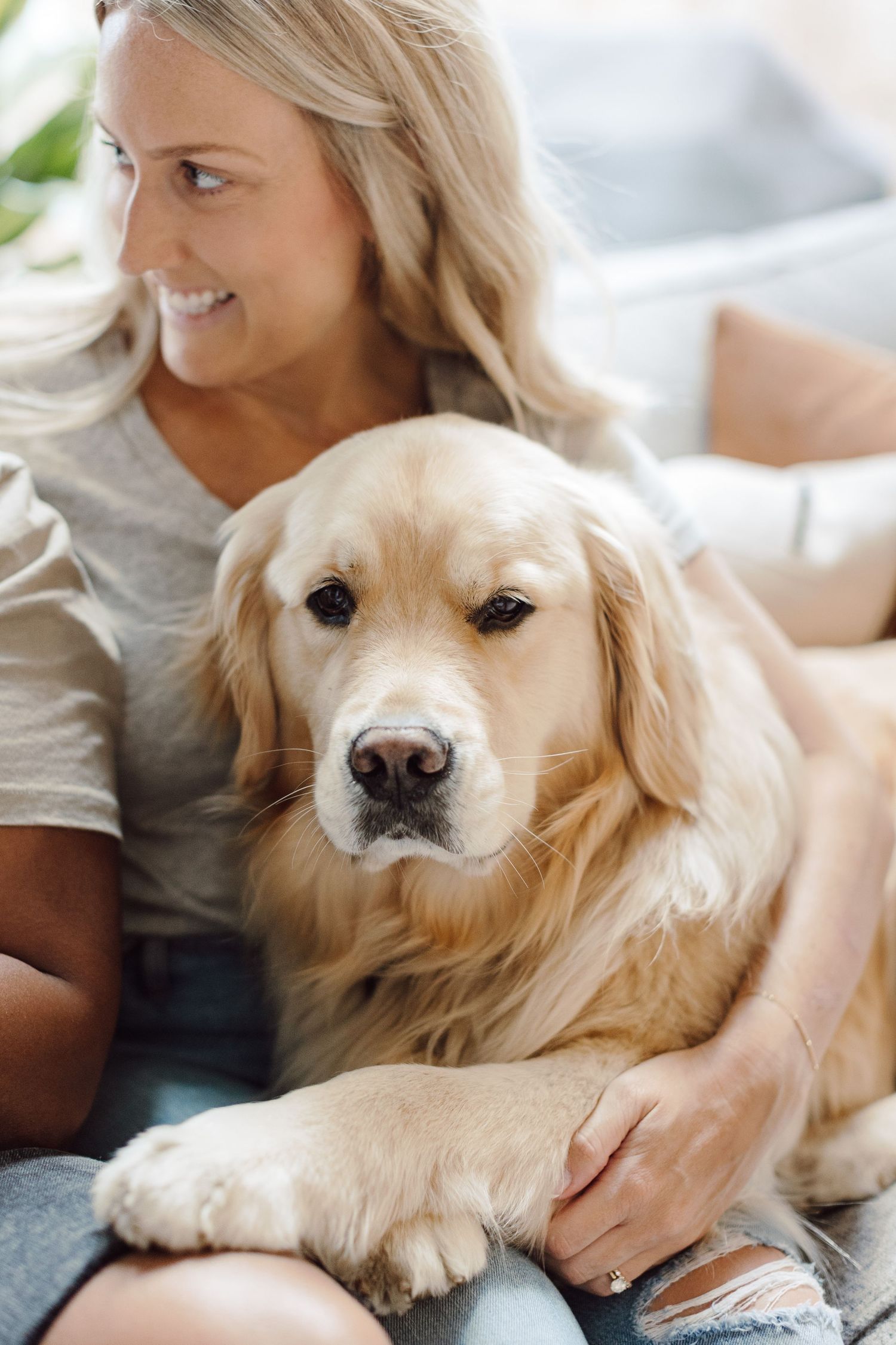 Woman cuddling with a golden retriever dog on a couch in natural light.