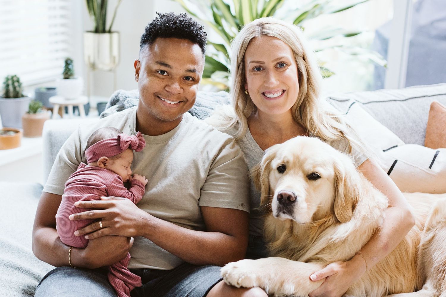 Couple relaxing on couch with their golden retriever dog in bright living room.