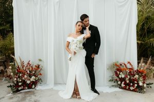 Elegant wedding couple embraces in front of white backdrop with pink and burgundy floral arrangements.
Cancún wedding photographer