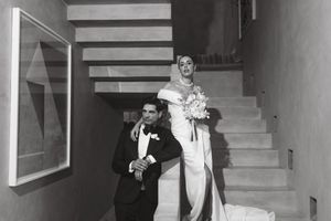 A black and white wedding photo showing a bride in a white dress descending stairs with attendants following behind.