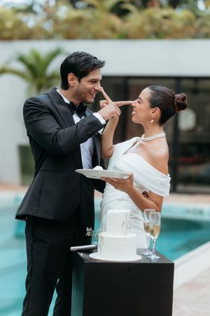 Newlyweds playfully feed each other wedding cake beside a pool during their outdoor reception celebration.
La Valise Tulum