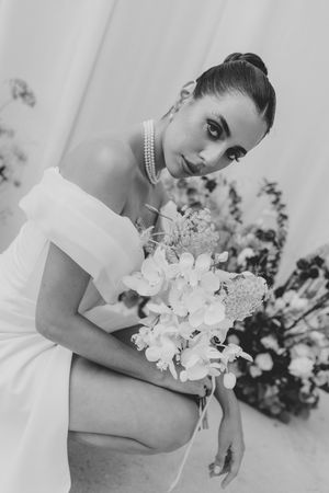 Black and white portrait of bride in off-shoulder dress holding white orchids, wearing pearl necklace.
Film wedding photographer