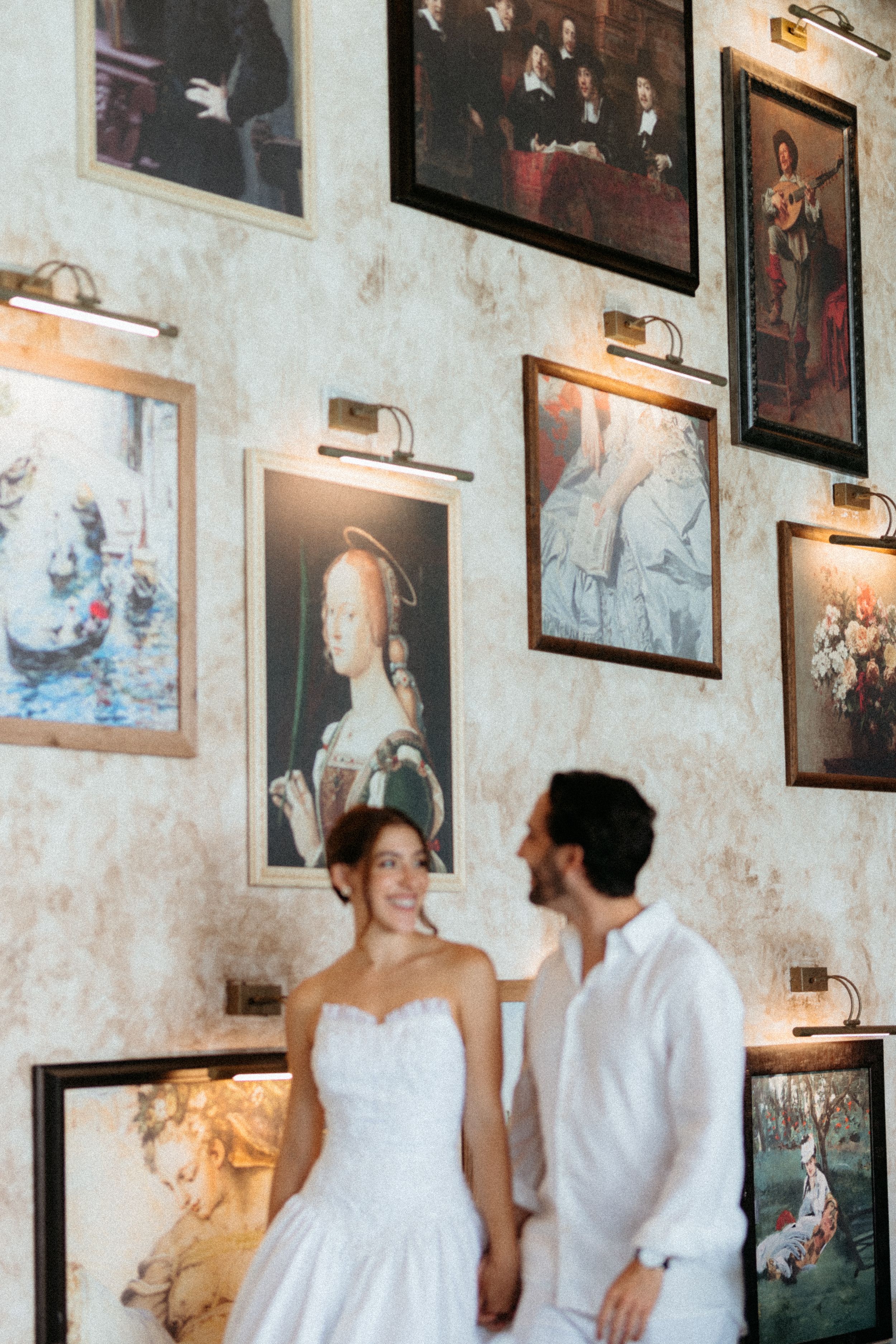 A couple in wedding attire stands together against a wall decorated with vintage portrait paintings and picture lights.
Amalfi Coast photo