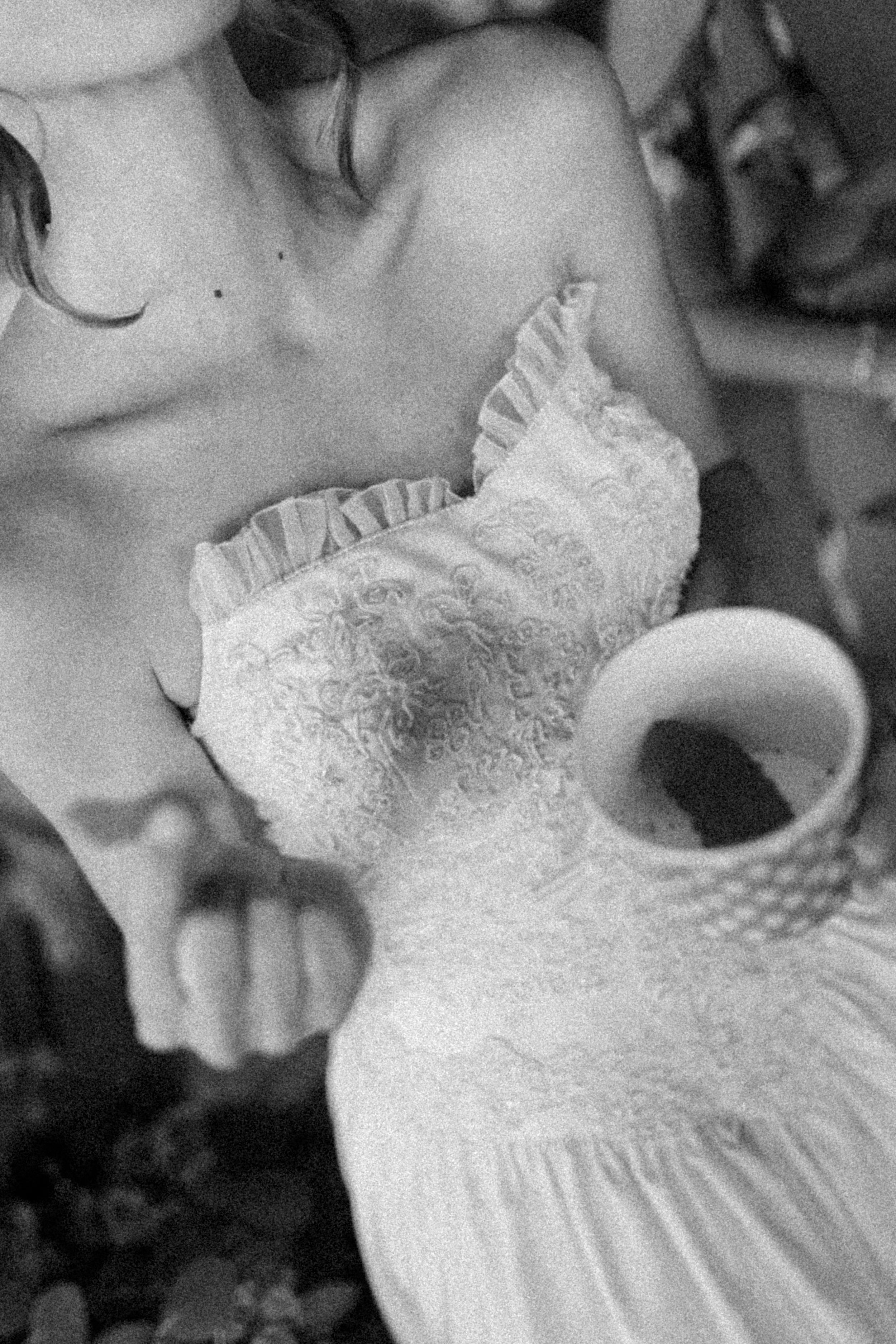 A black and white close-up photo showing a delicate white lace christening gown with intricate details and ruffles.
Film wedding photographe