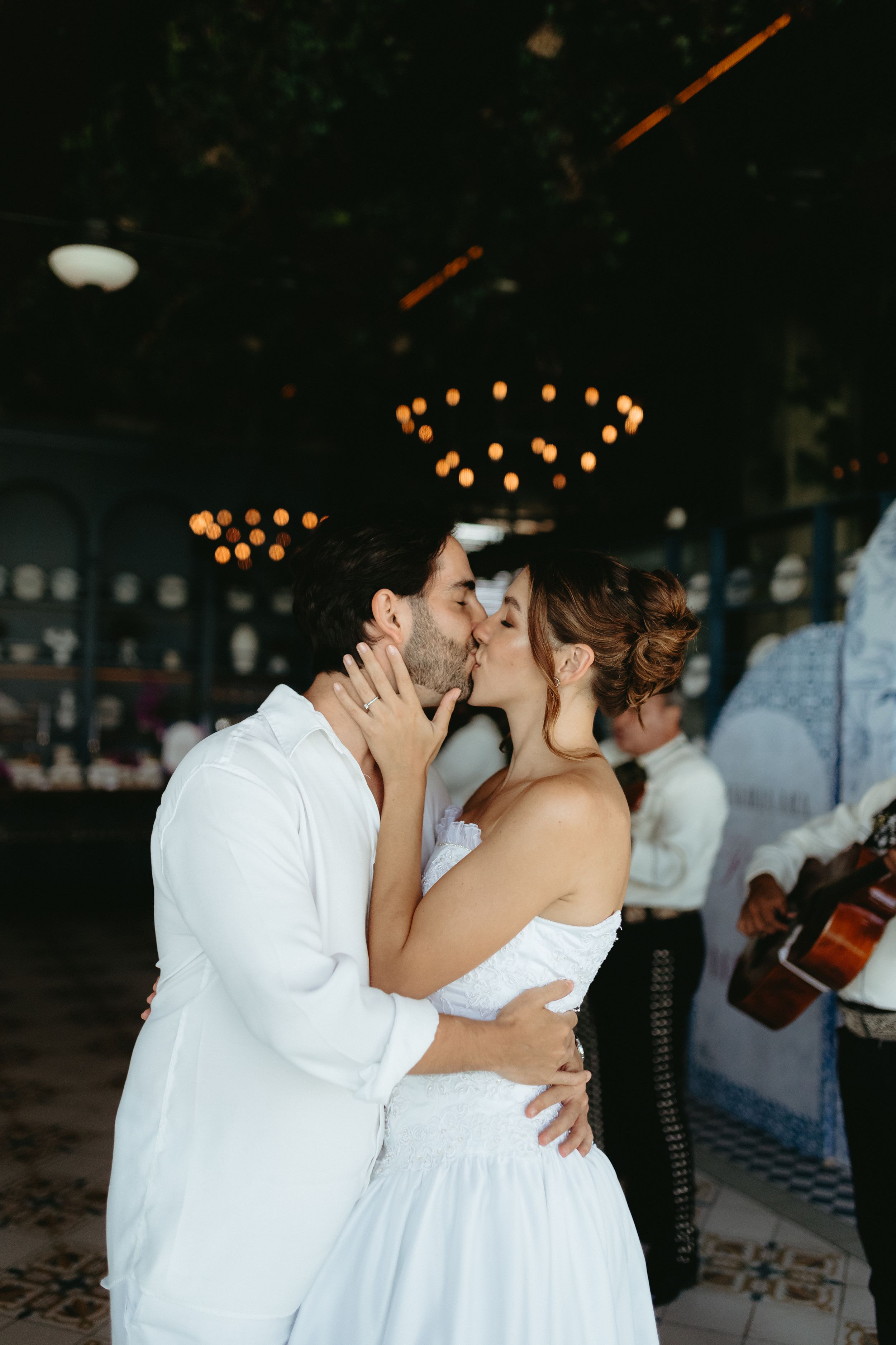 A romantic wedding moment captured in a sequence of photos showing a couple in white attire sharing a kiss under string lights.
Mexico