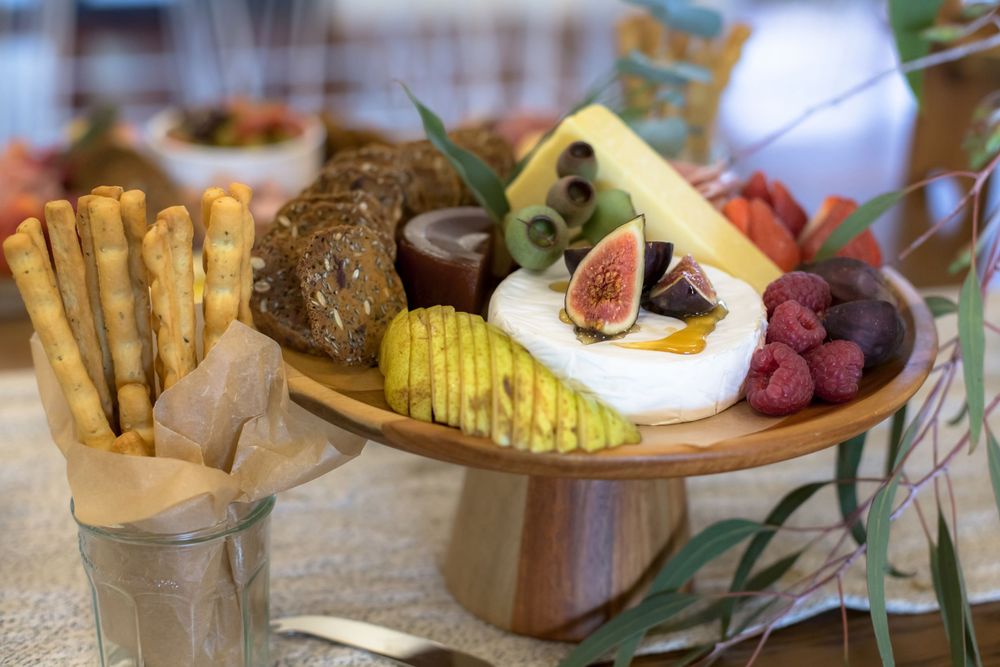 Artisanal cheese board with breadsticks, figs, raspberries and wavy potato chips served on wooden platter.