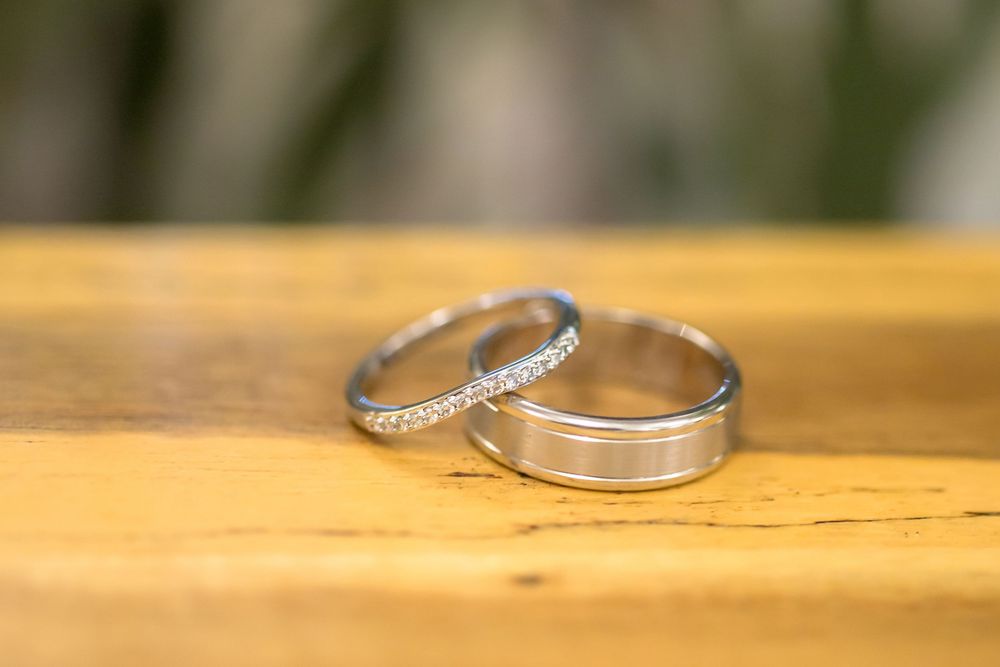 Two wedding bands rest on a wooden surface, one plain silver and one adorned with small diamonds.
