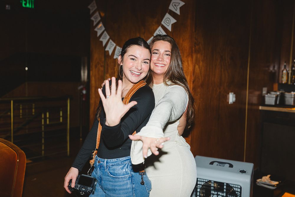 People dancing and embracing in a dimly lit room during what appears to be a social gathering or party.