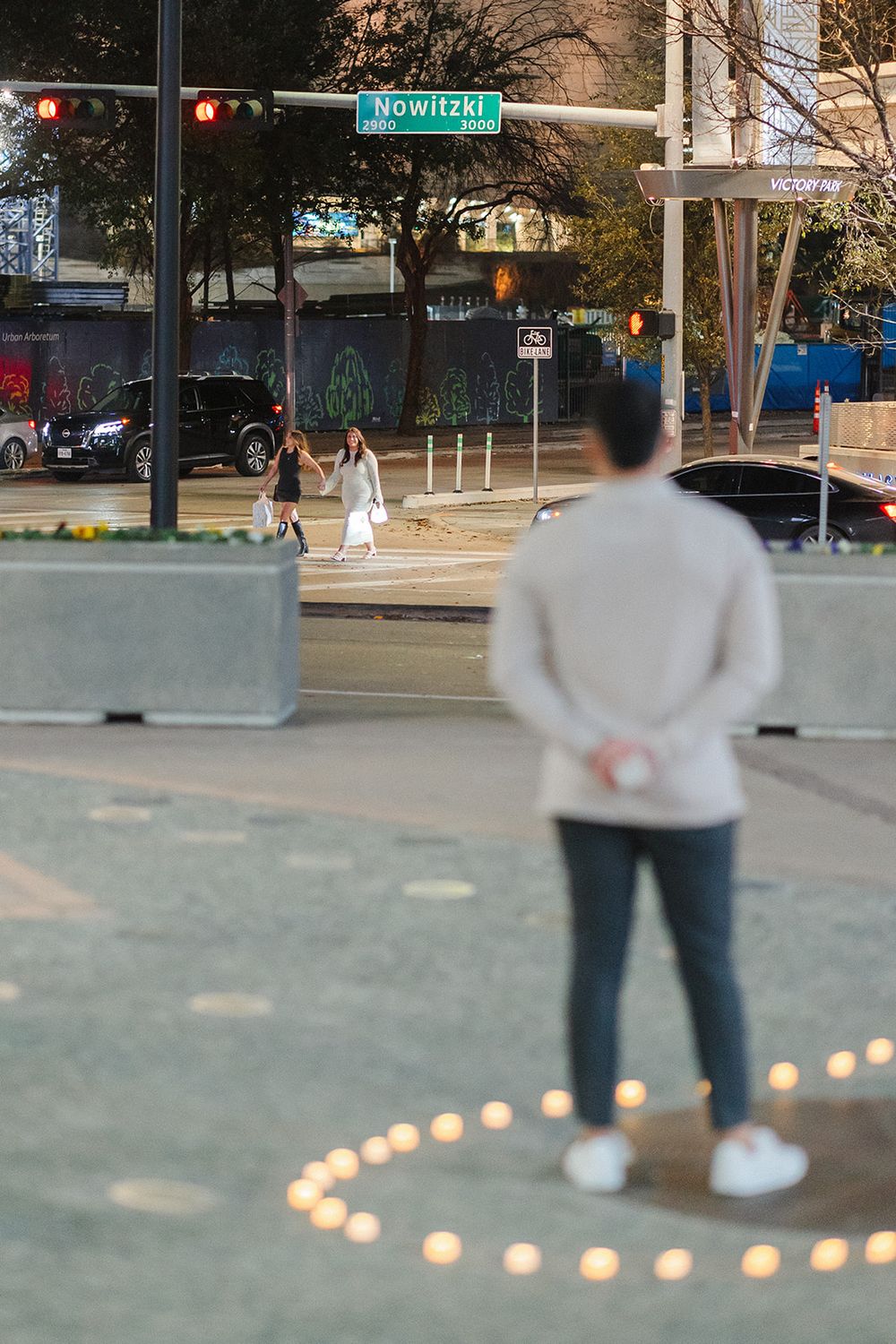 A row of glowing candles creates a path on a concrete surface at dusk with a street sign visible in the background.