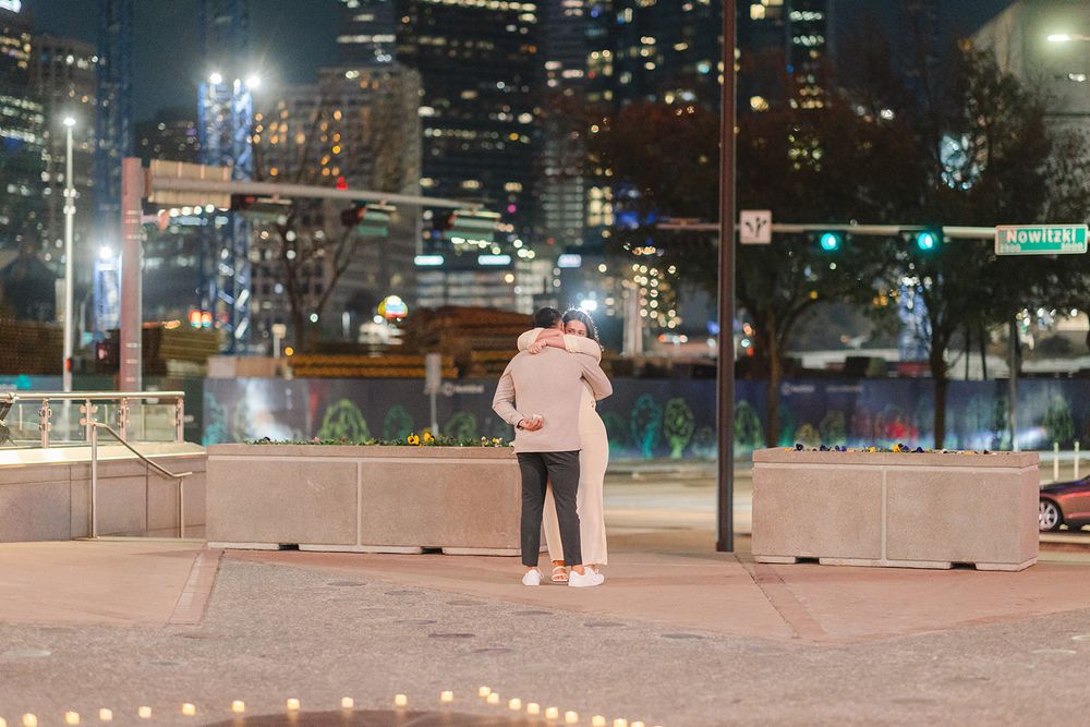 People playing pickleball at an outdoor court illuminated by bright lights at night in an urban setting.