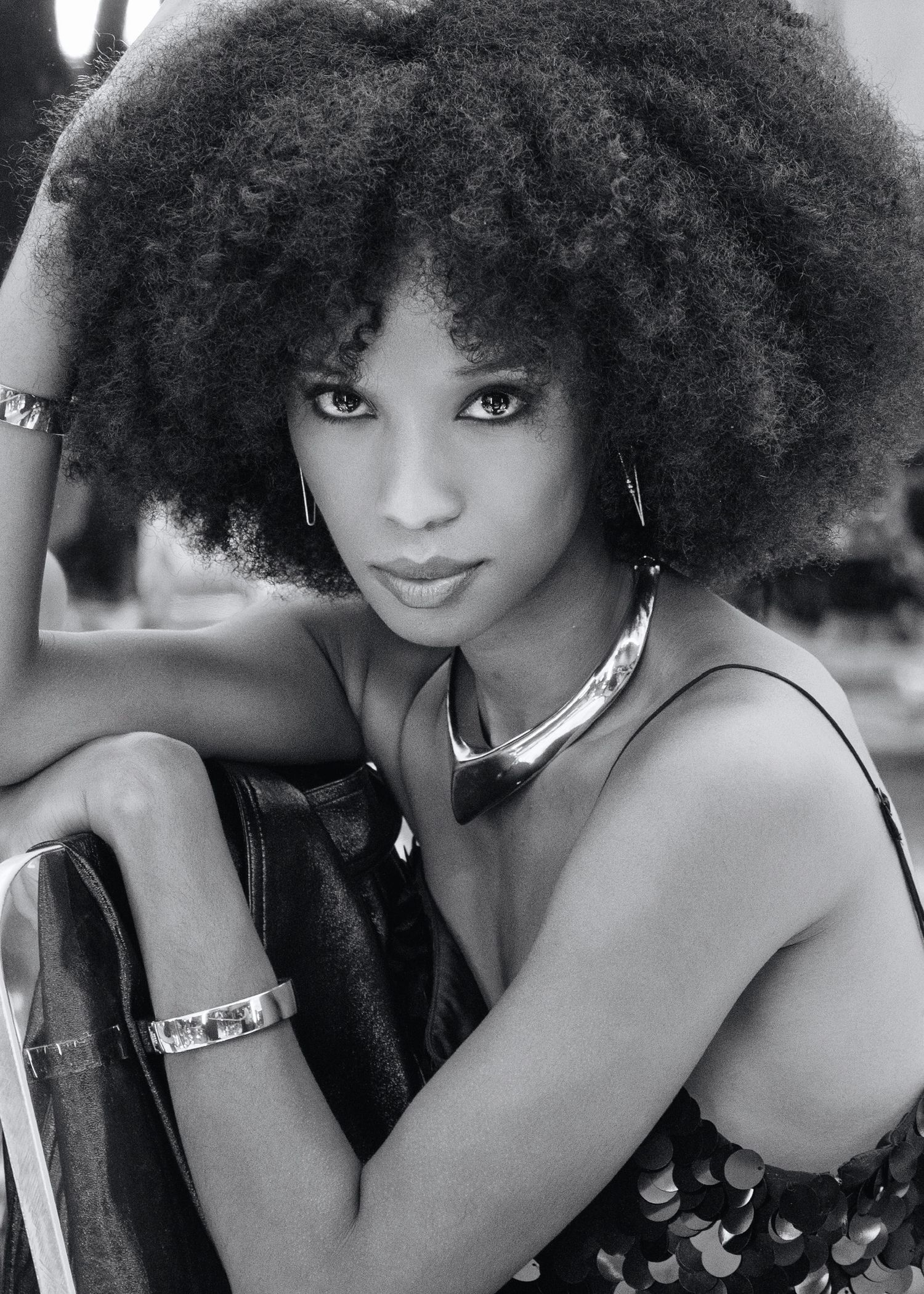 Black and white portrait of a woman with a natural afro hairstyle wearing silver jewelry and a dark top.