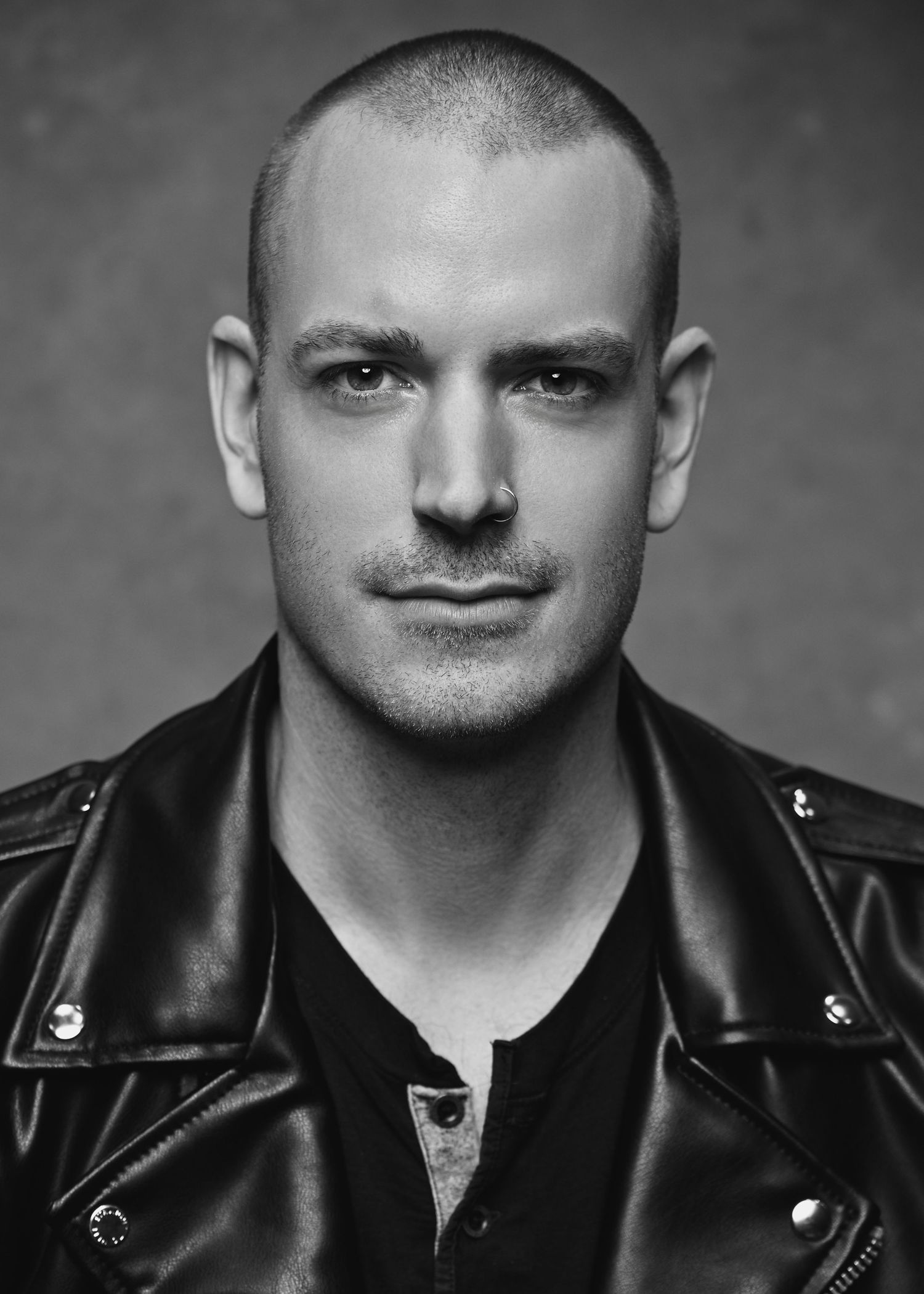 Black and white portrait of a bald man in a leather jacket with an intense gaze.