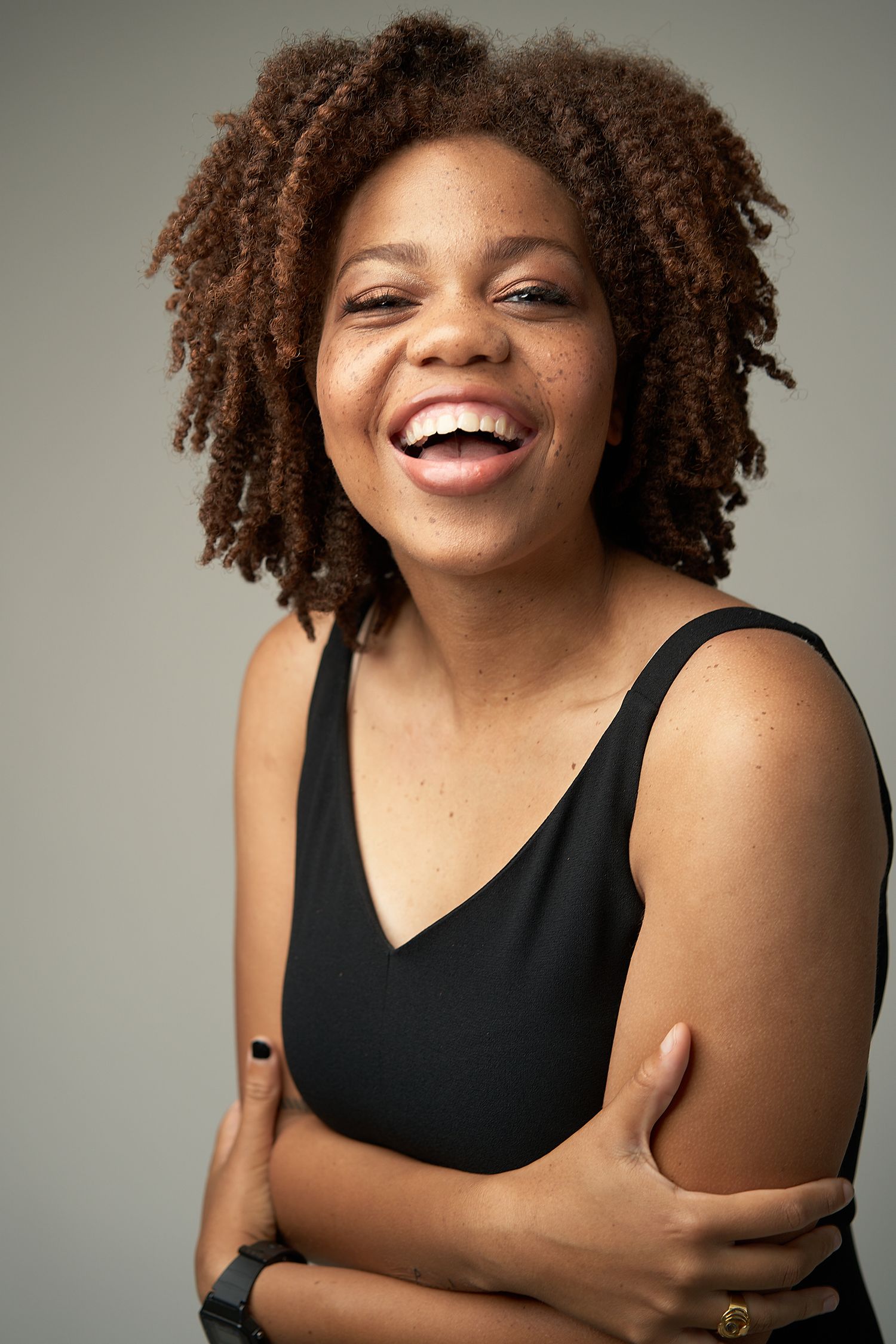 Joyful young Black woman with natural hair laughs warmly in a black sleeveless top.