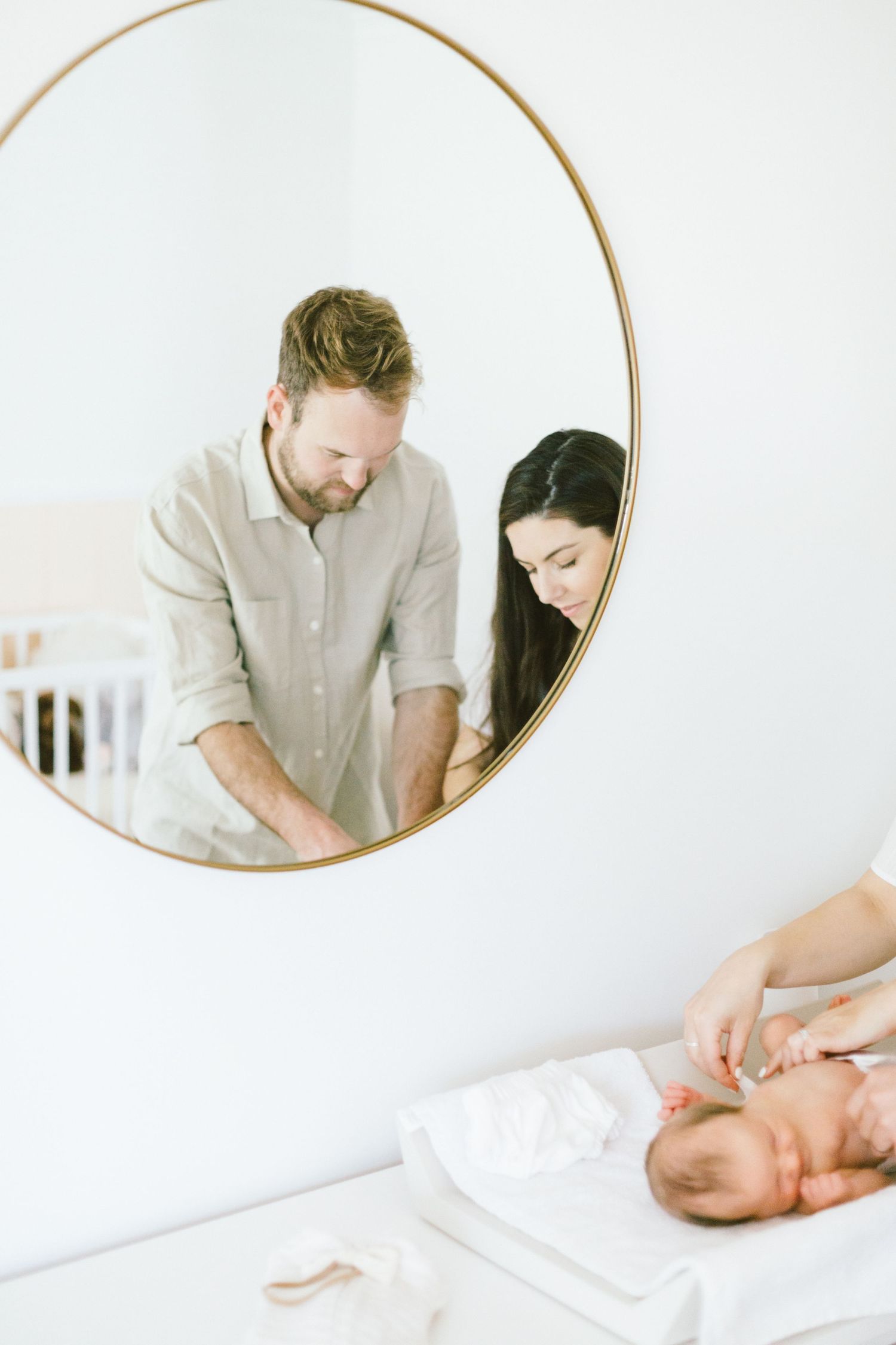 Circular mirror reflection showing a couple caring for their baby on a changing table.