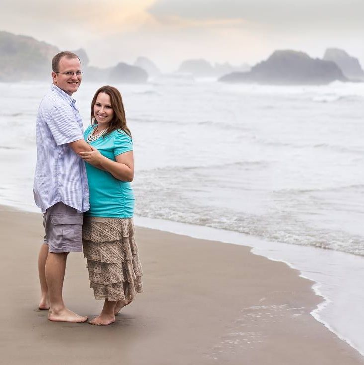 Couple walking barefoot along beach shoreline at sunset.