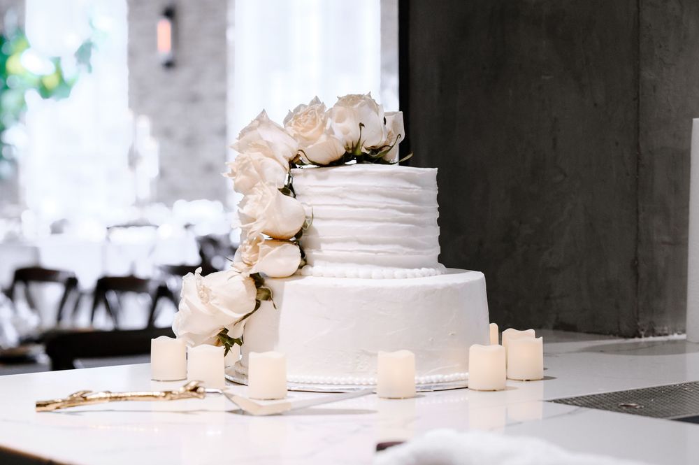 White tiered wedding cake decorated with delicate white flowers and roses displayed at an elegant reception.