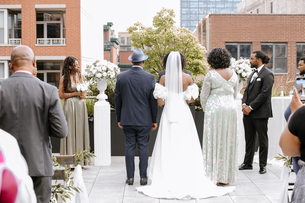Outdoor wedding ceremony on a rooftop terrace surrounded by brick buildings and floral arrangements.
