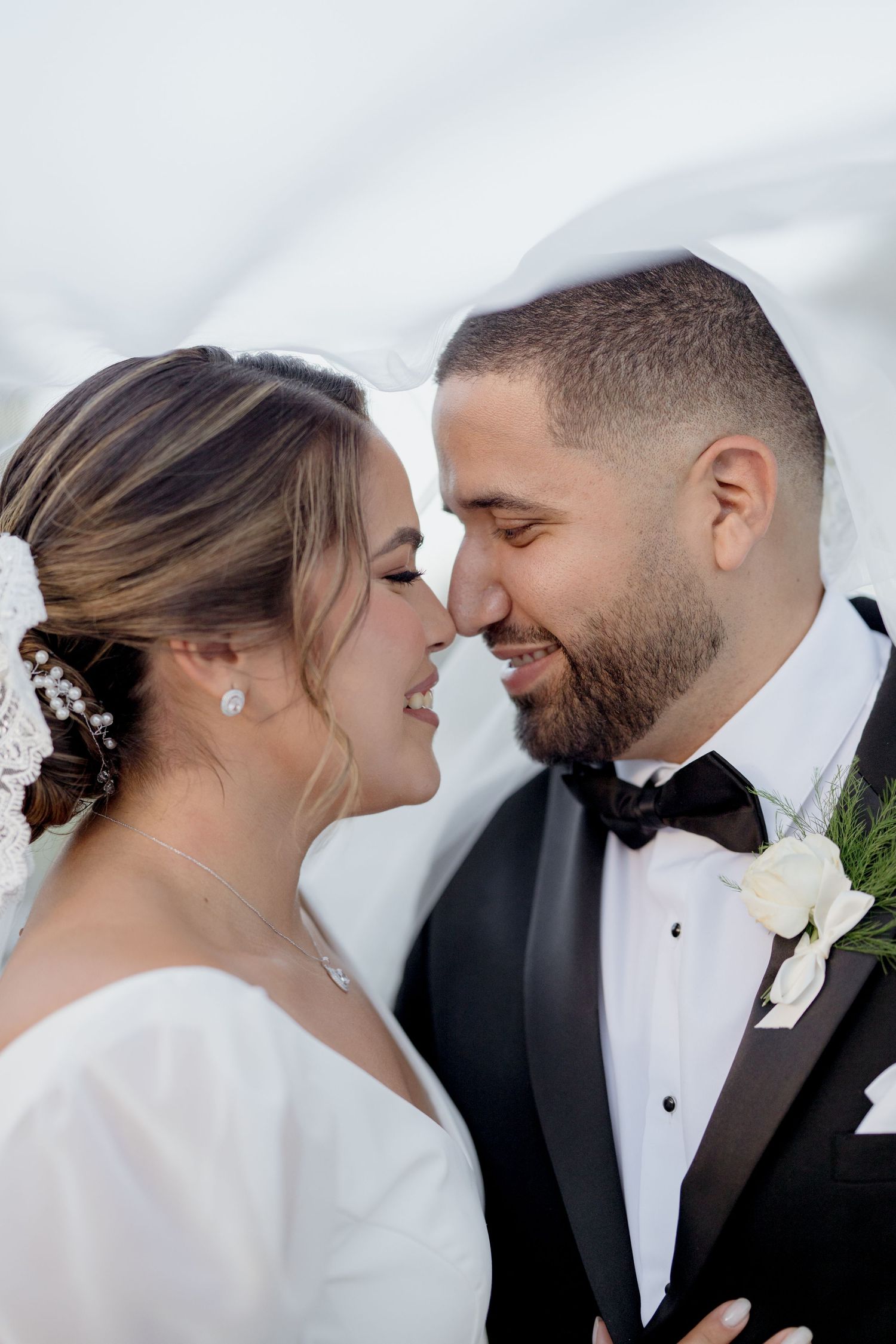 Intimate wedding portrait of newlywed couple sharing a close romantic moment against a soft white background.
