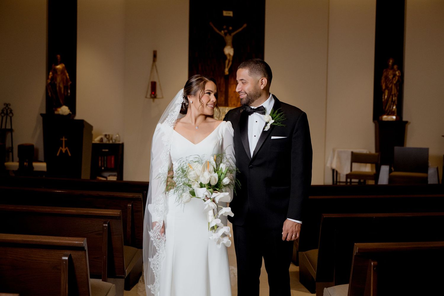 A couple shares an intimate moment at their wedding ceremony in a traditional church sanctuary with wooden pews.