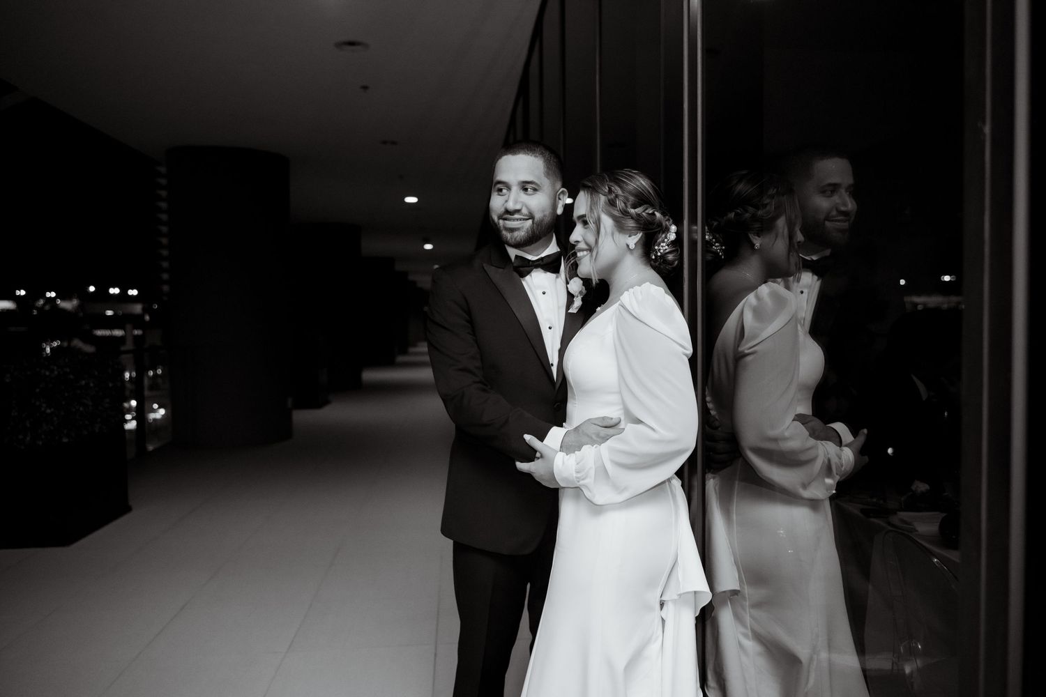 Silhouetted wedding couple embraces in front of bright doorway during evening reception.