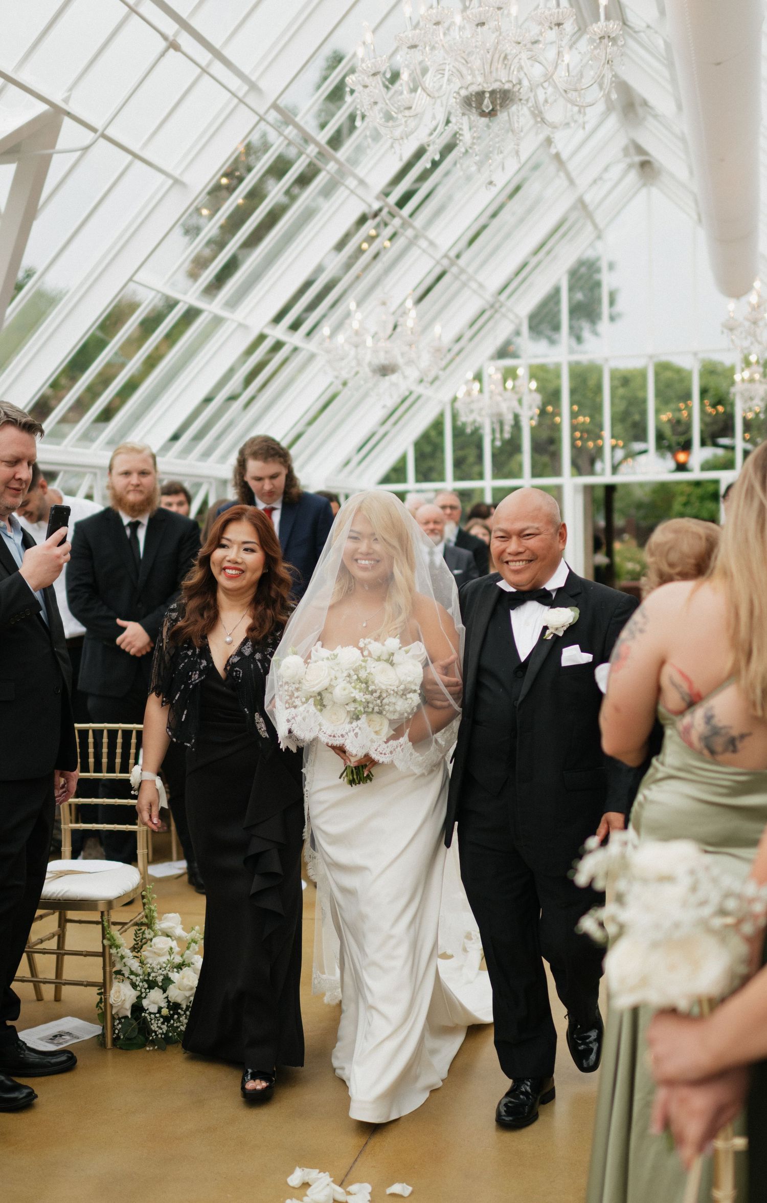 A joyful wedding ceremony in a sunlit greenhouse with guests gathered around the happy couple.